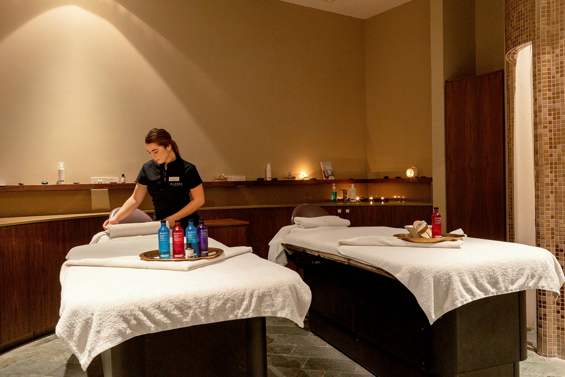 Ett spa-rum med två massagestolar täckta med vita dukar och produkter på brickor. (AI-genererad text)