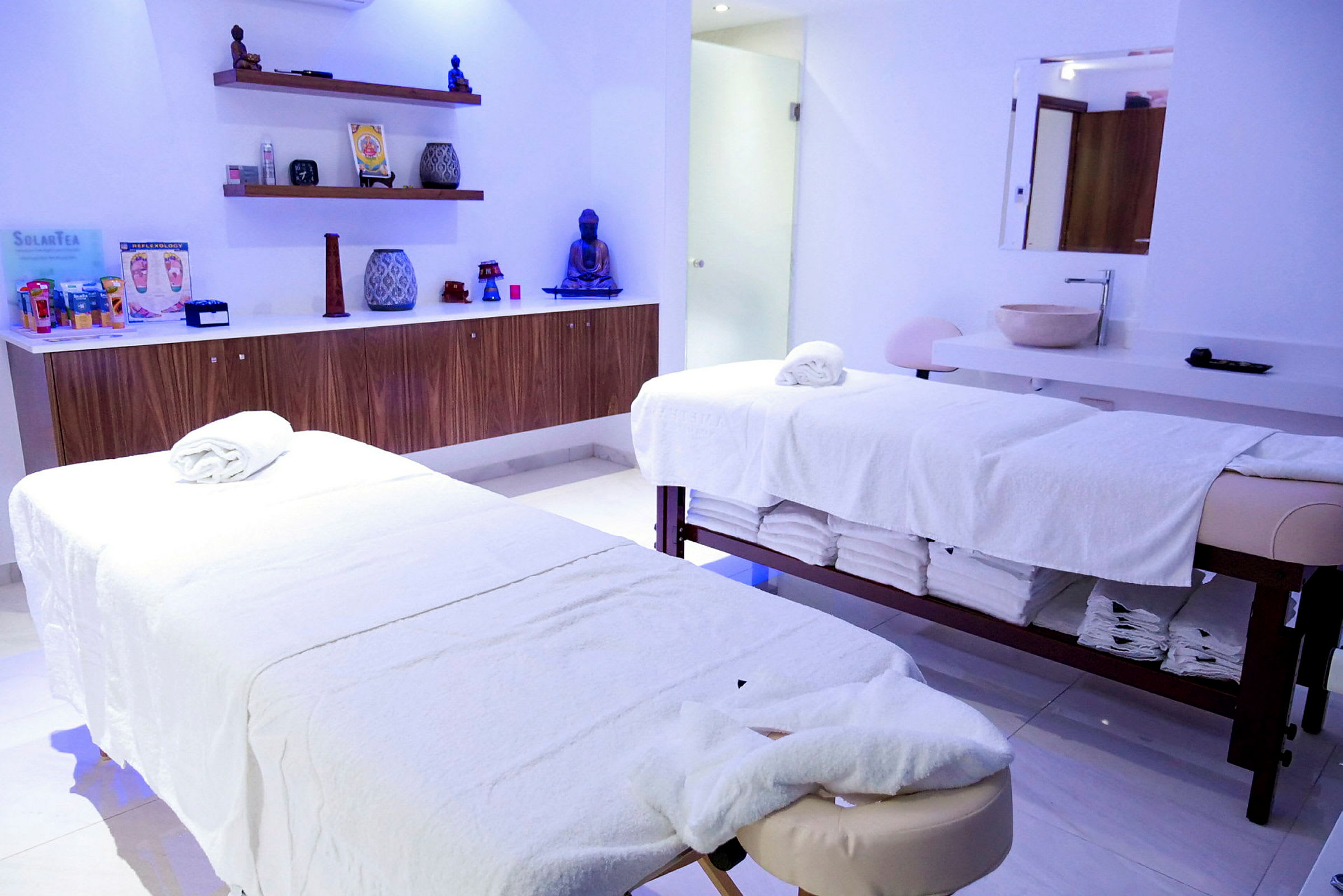 Ett ljus och stilrent behandlingsrum med två massagebänkar täckta med vita handdukar. (AI-genererad text)