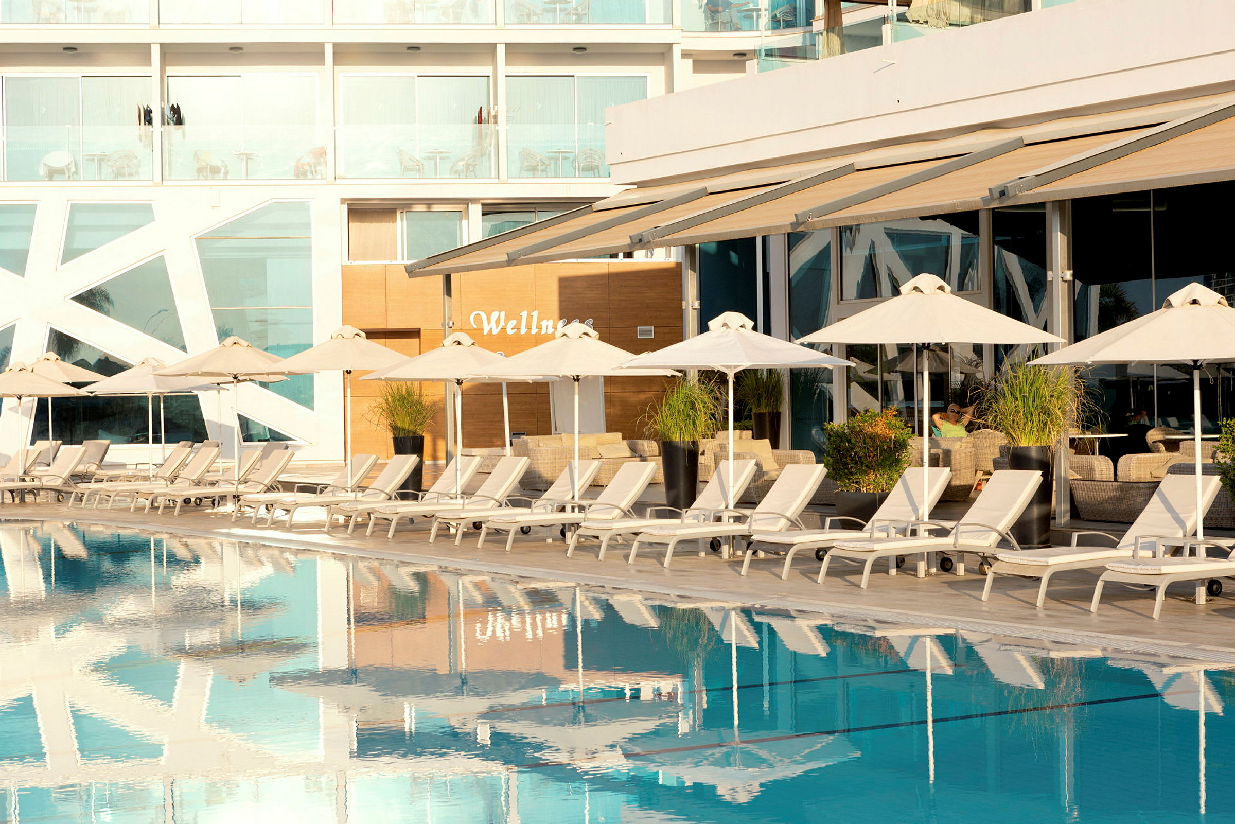 Poolområde med solstolar och parasoller framför en modern byggnad. (AI-genererad text)