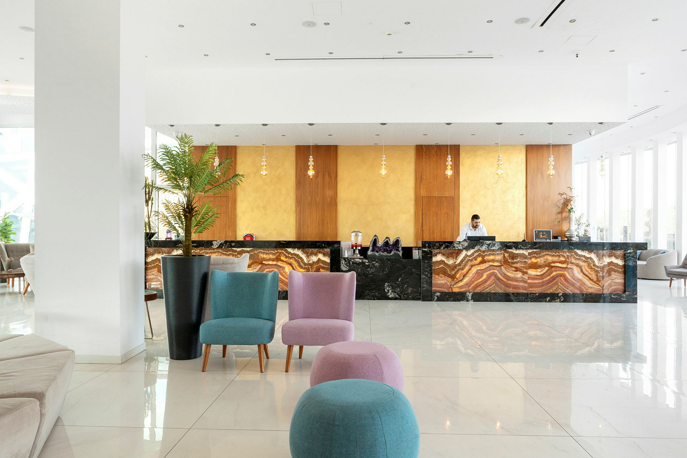 Ett hotellreceptionsområde med en marmorerad receptionsdisk, färgglada sittplatser och dekorativa växter. (AI-genererad text)