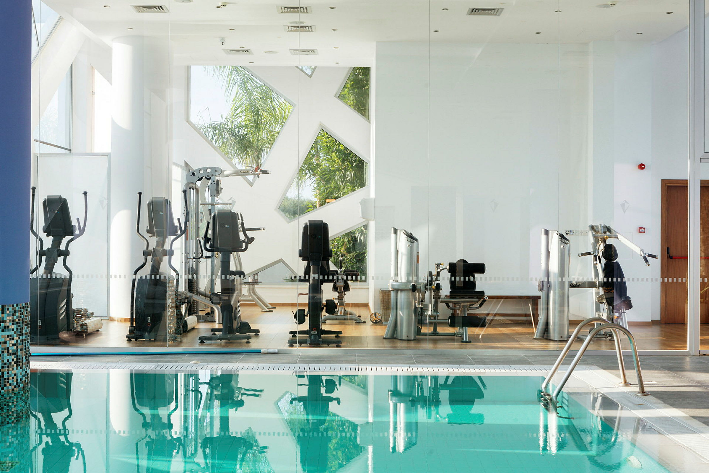 Bild av gymutrustning bakom glasväggar nära en pool. (AI-genererad text)