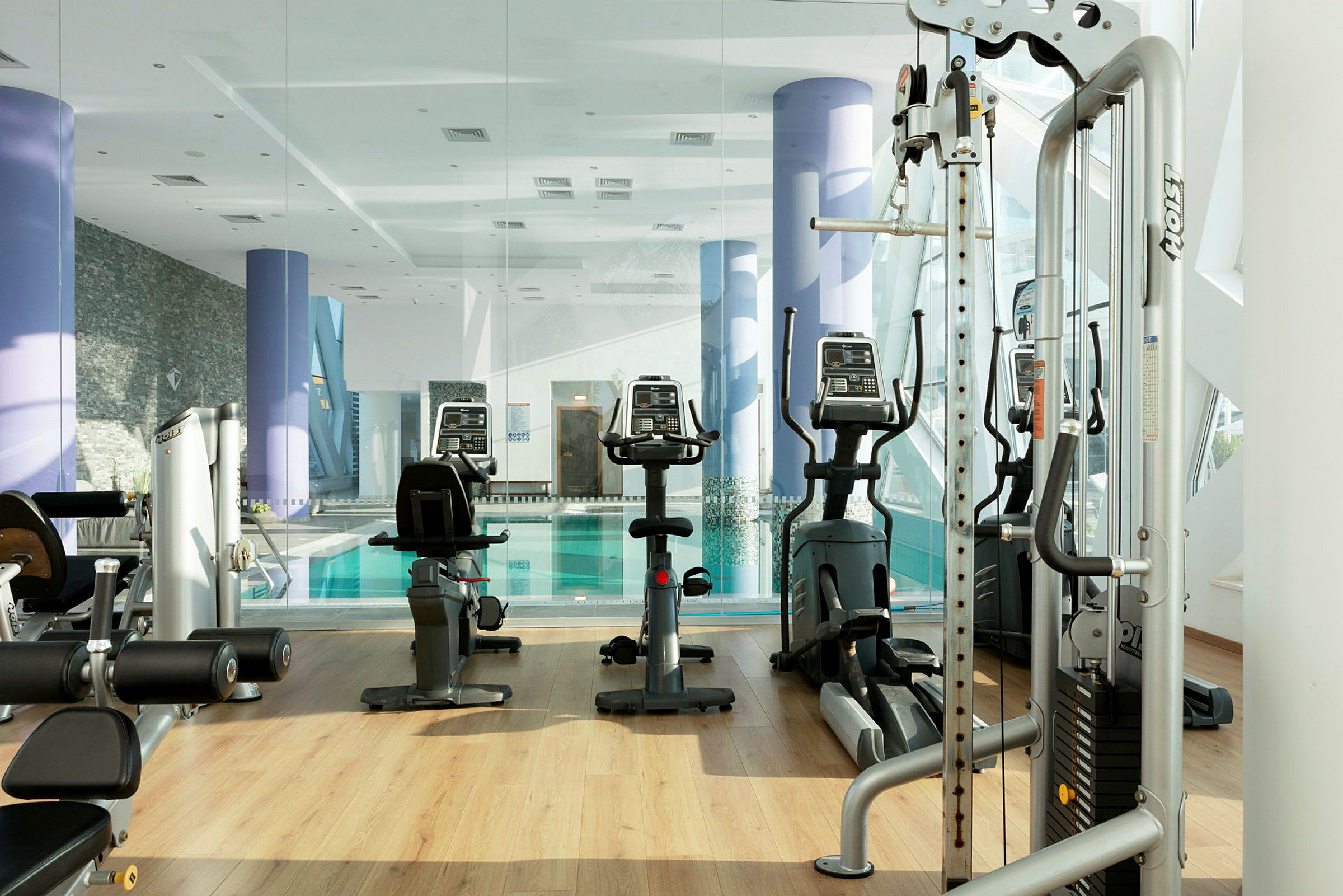 Ett gym med träningsmaskiner och utsikt mot en inomhuspool. (AI-genererad text)