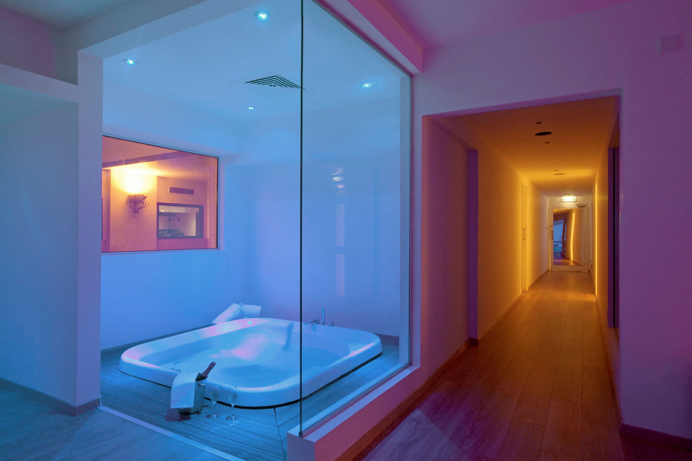 Ett modernt badrum med jacuzzi belyst i blått och en angränsande korridor. (AI-genererad text)