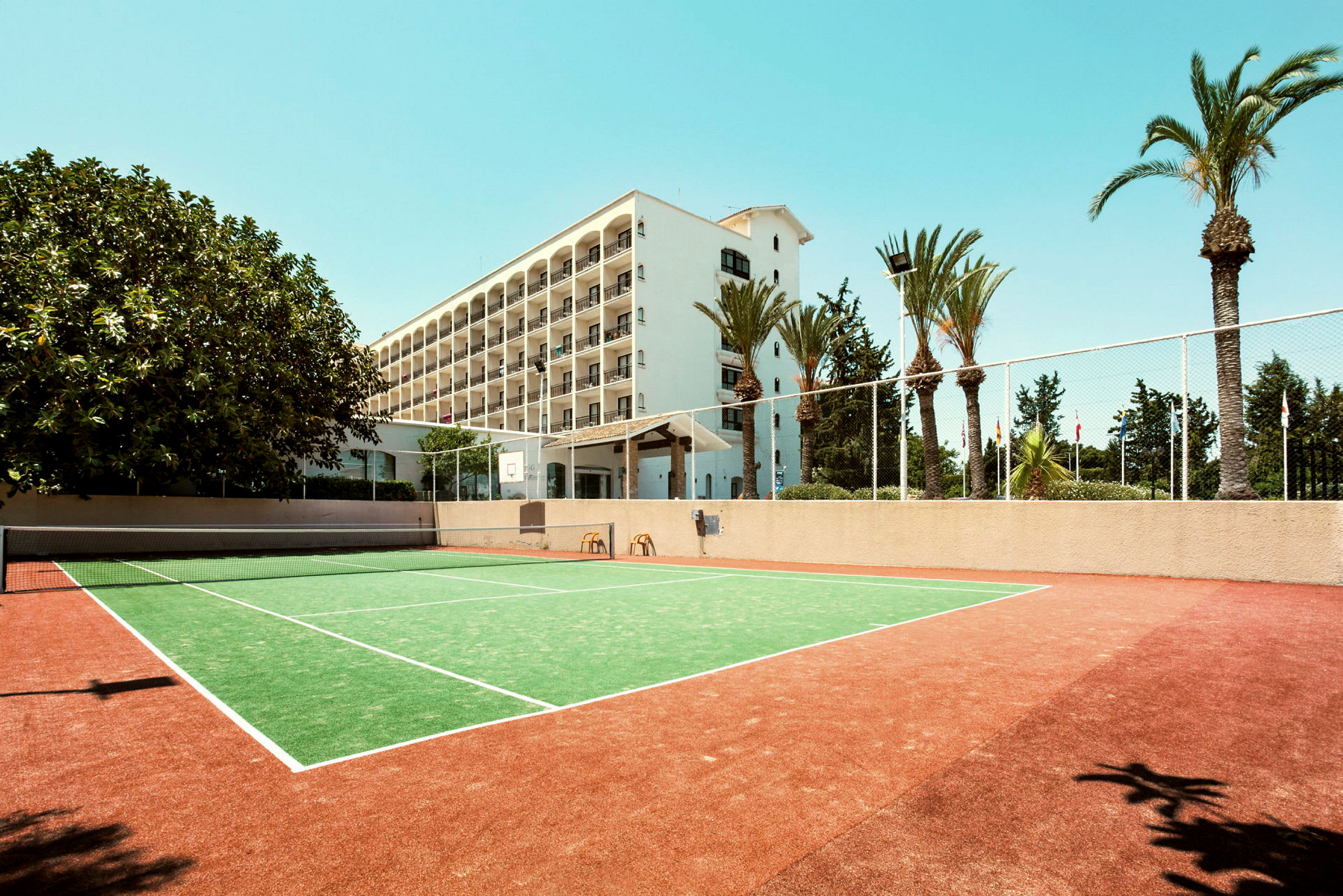 En tennisbana framför ett hotell med flera våningar och omgivande palmer. (AI-genererad text)