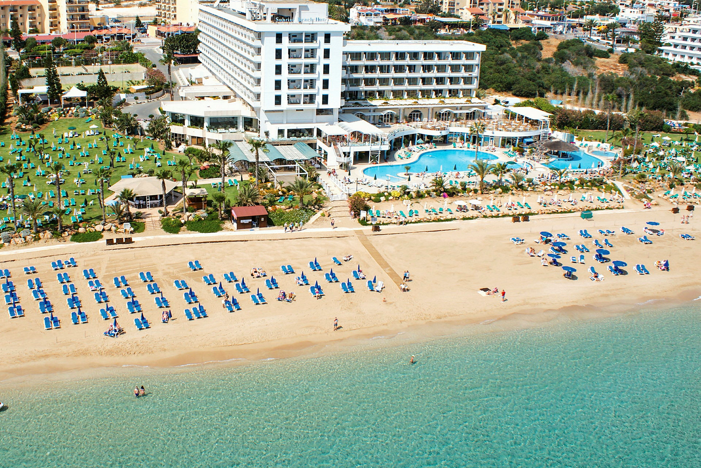 Strand med solstolar och parasoller framför hotell med poolområde. (AI-genererad text)