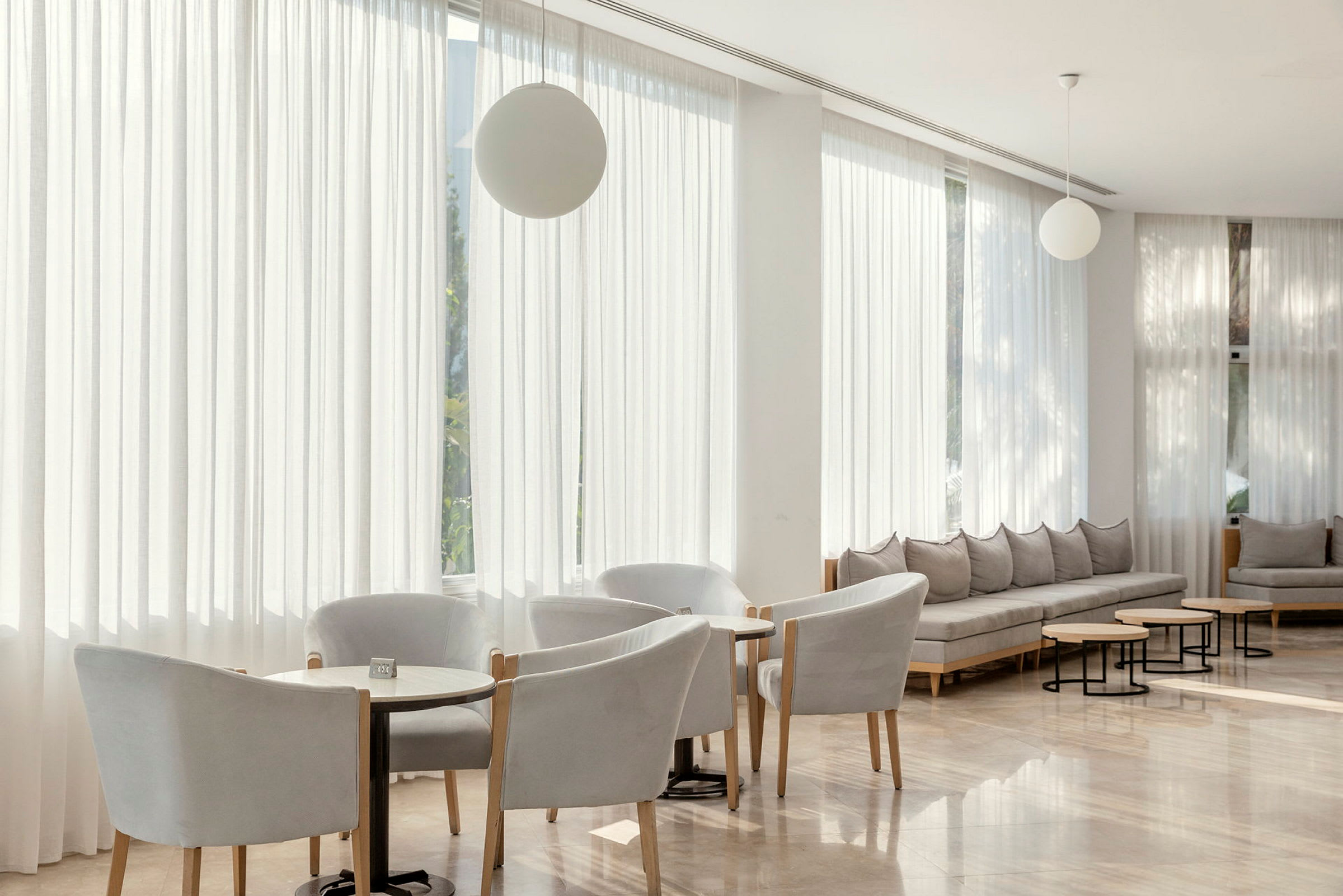En modern lounge med stolar, små bord och soffor i ljusa färger. (AI-genererad text)