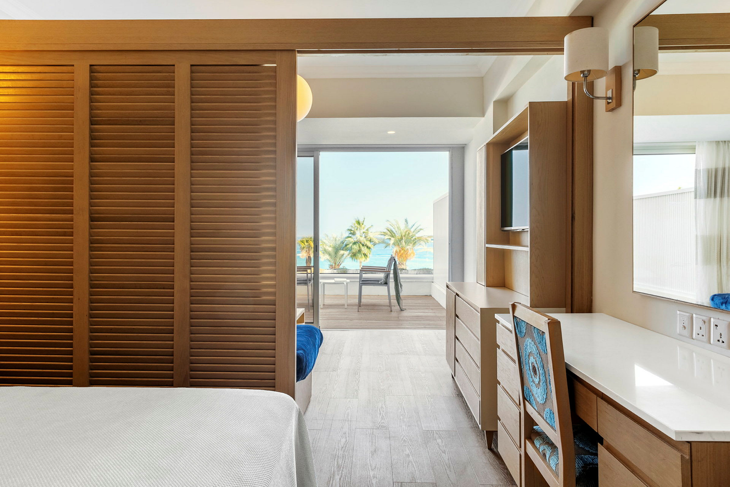 Ett ljust hotellrum med utsikt över havet och palmer genom stora fönster. (AI-genererad text)