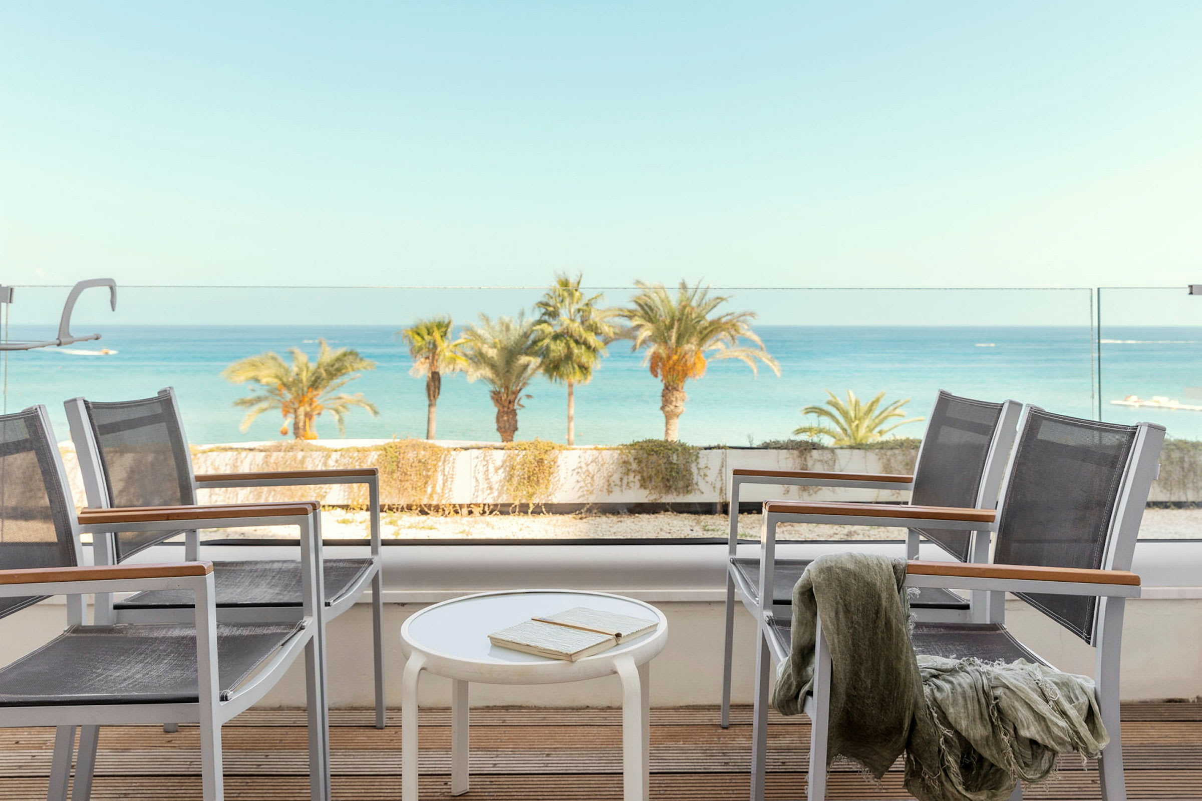 Utsikt från en terrass med stolar, bord, och havet i bakgrunden. (AI-genererad text)