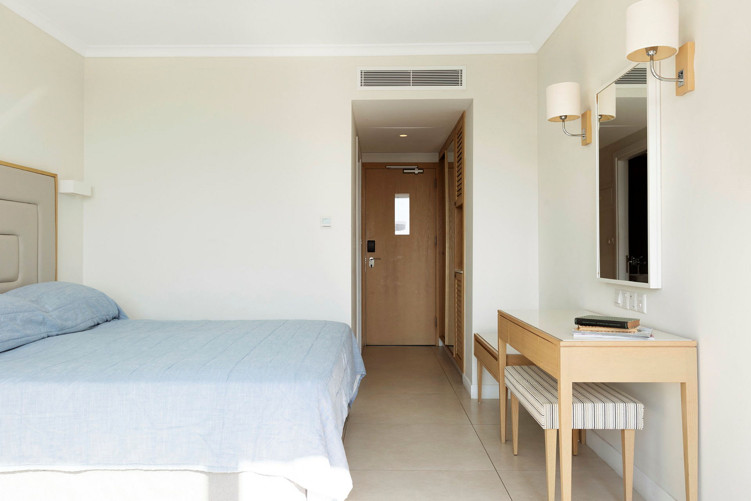 Ett hotellrum med en säng, en spegel och ett skrivbord. (AI-genererad text)