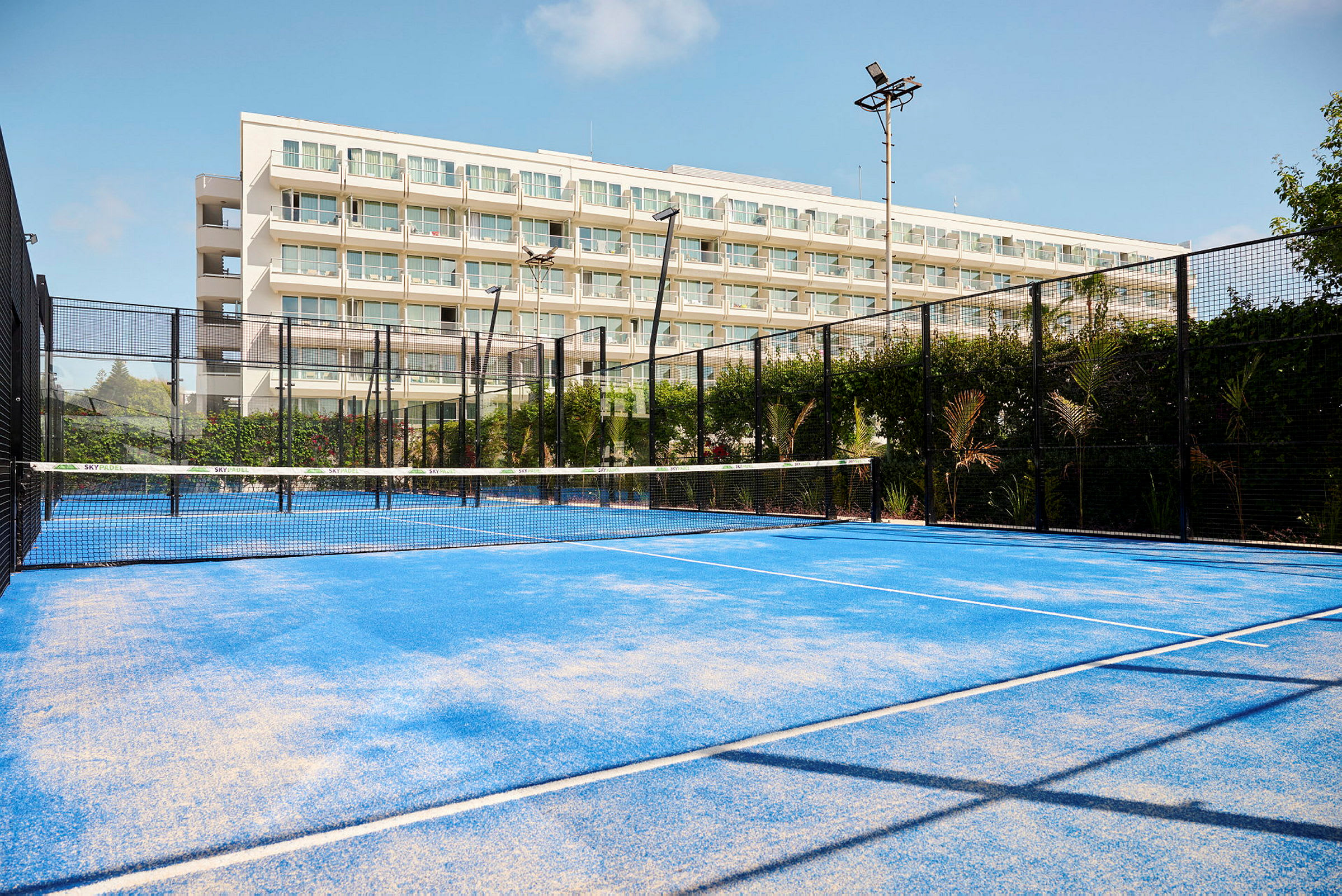 En padelbana med blått underlag framför en byggnad med balkonger. (AI-genererad text)