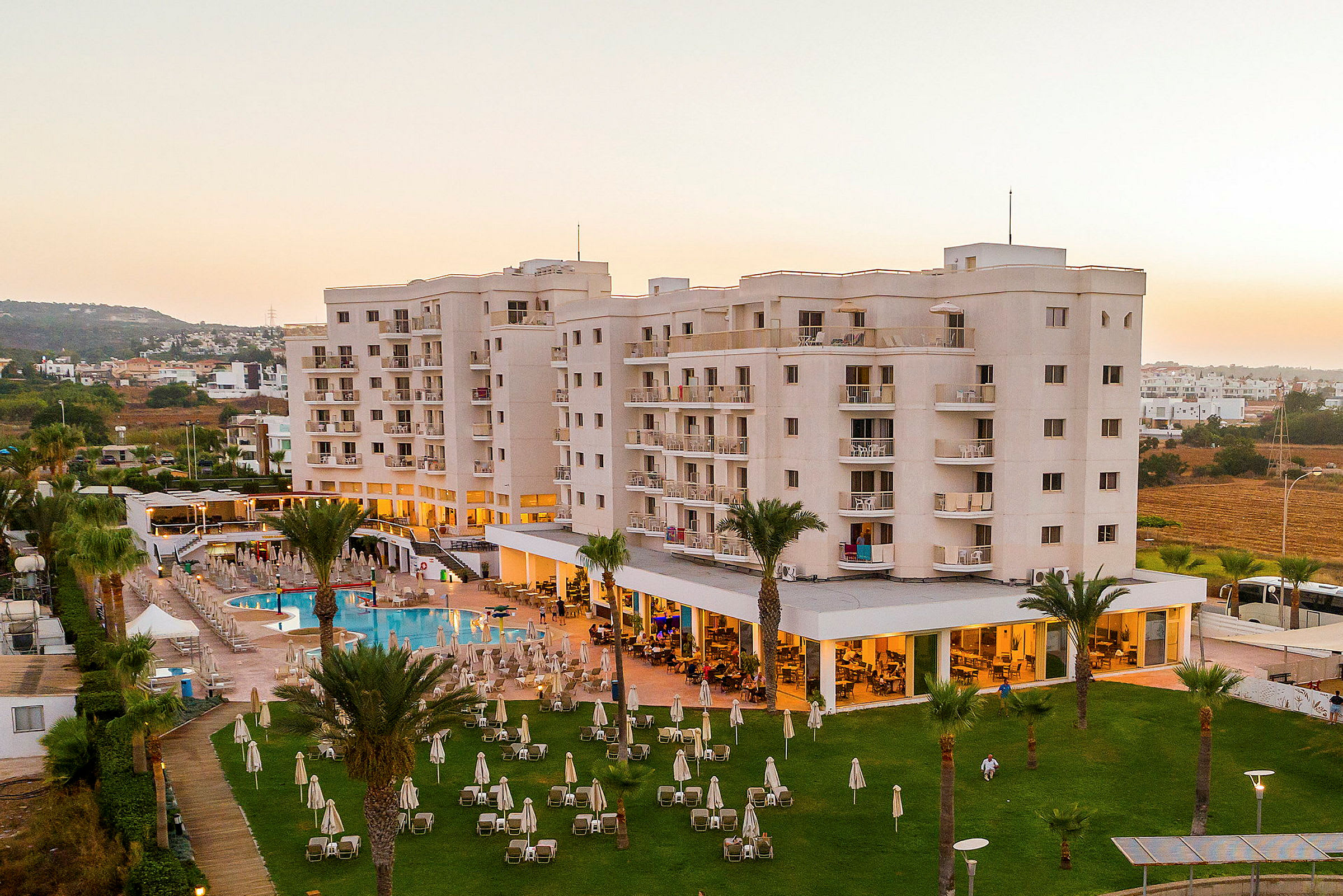 Flygfoto av ett hotell med balkonger, en pool och grönområde med solstolar. (AI-genererad text)