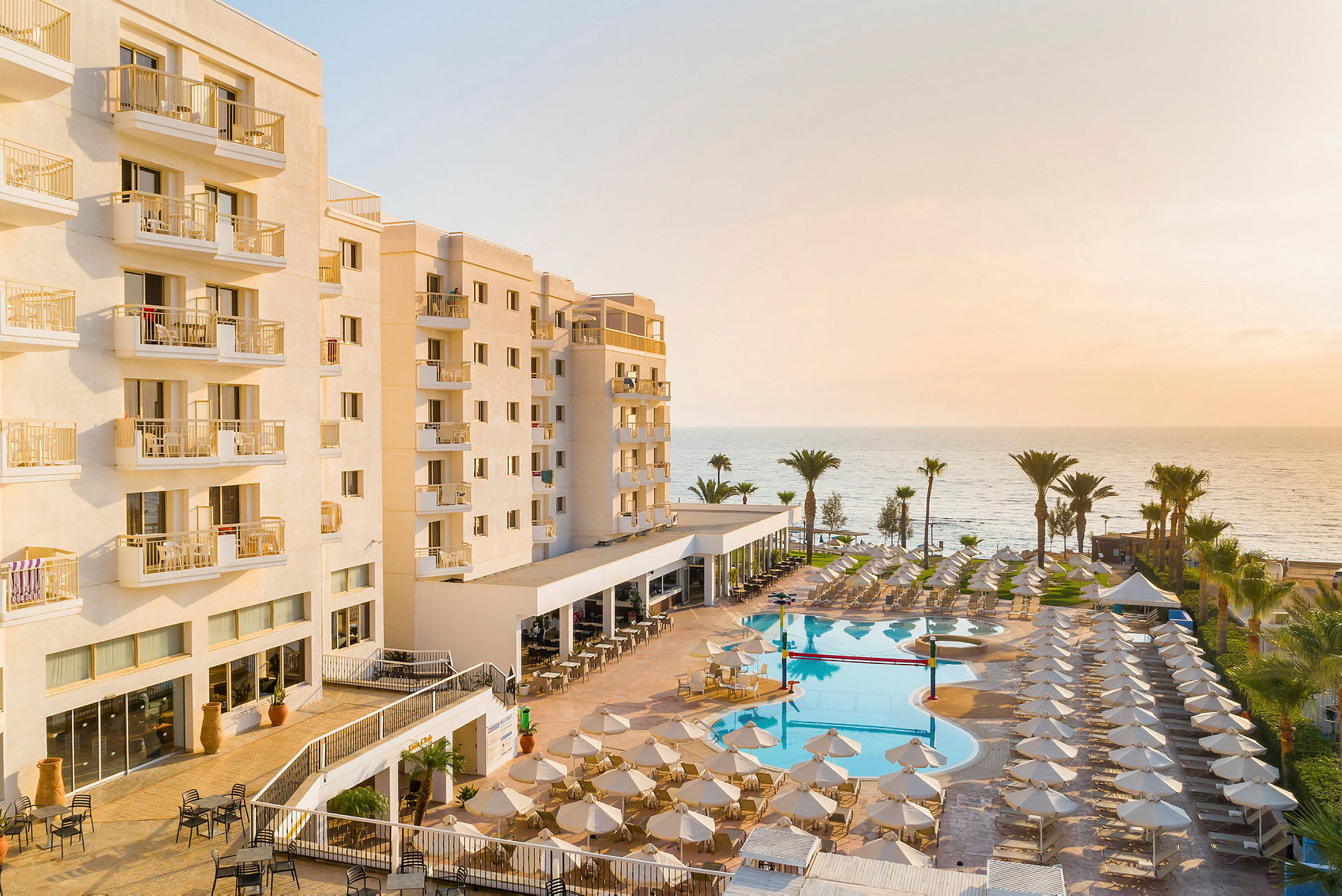 Hotellbyggnad med balkonger, pool och solstolar vid stranden. (AI-genererad text)