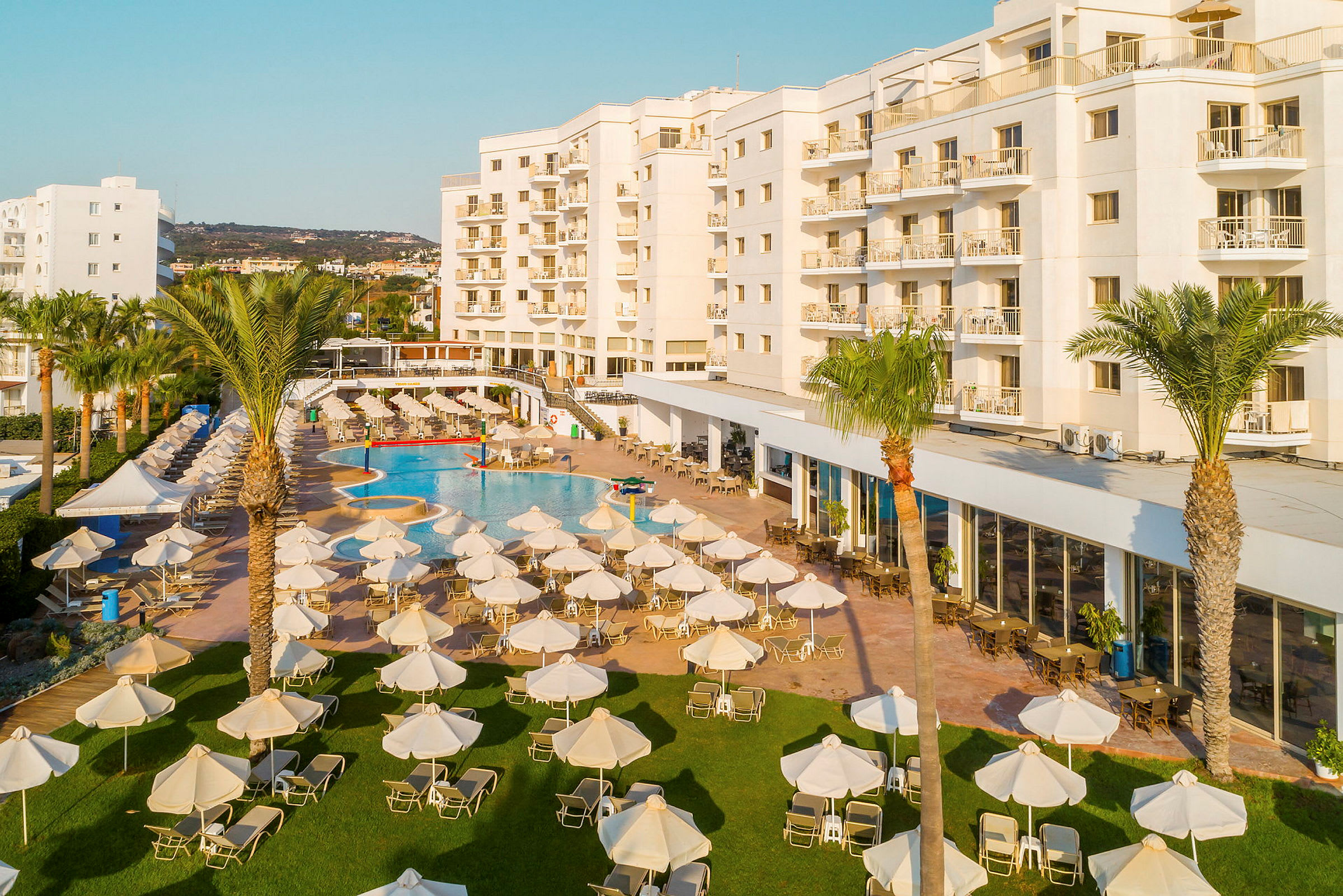 Hotellbyggnad med en stor pool och solstolar på grönyta. (AI-genererad text)