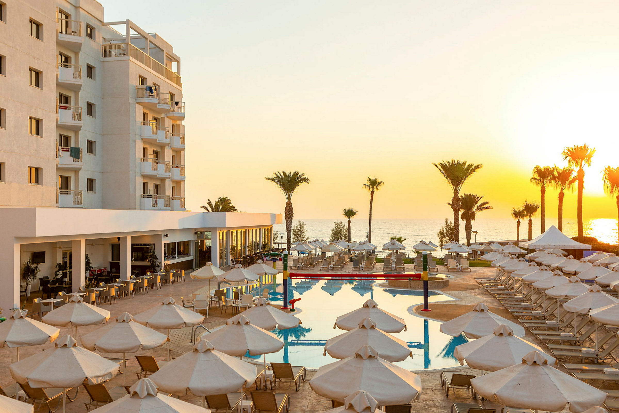 Hotellområde med pool, solstolar och parasoller nära havet vid solnedgång. (AI-genererad text)