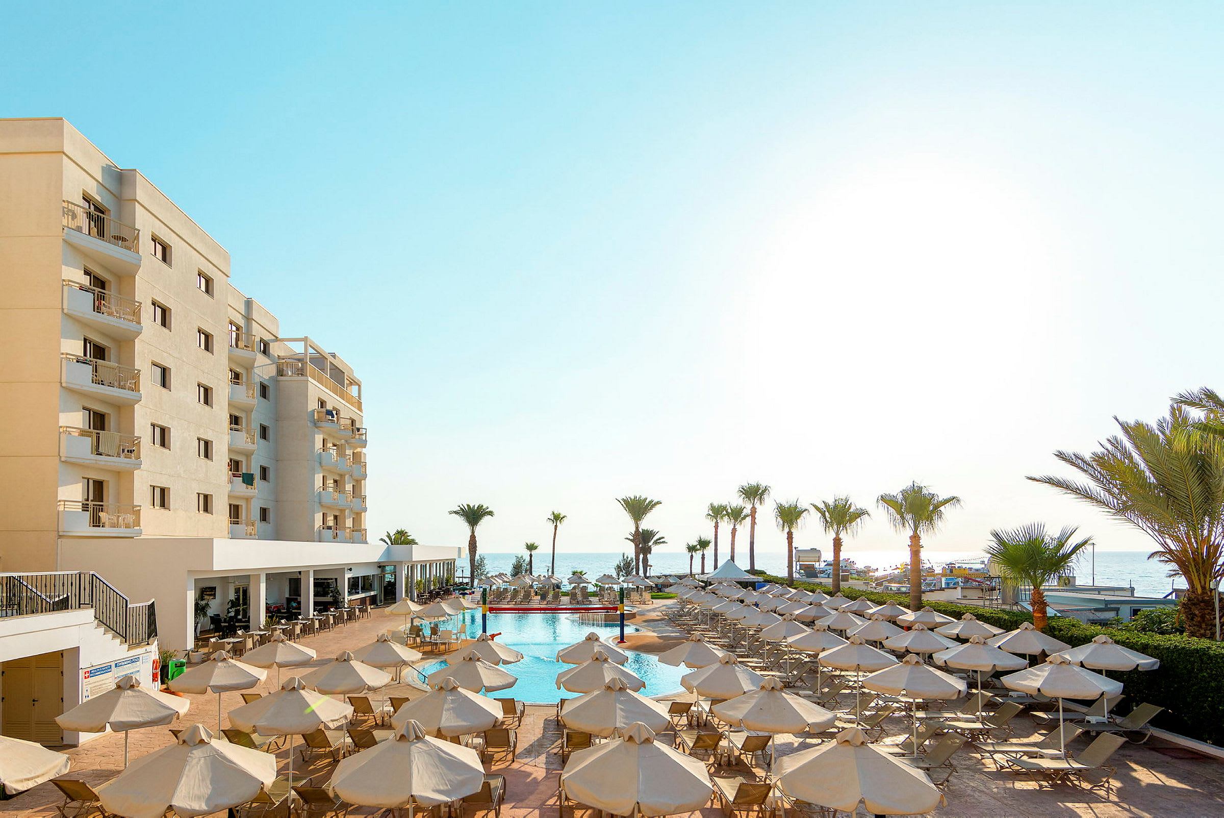 Hotell med poolarea och solstolar, palmer och havet i bakgrunden. (AI-genererad text)