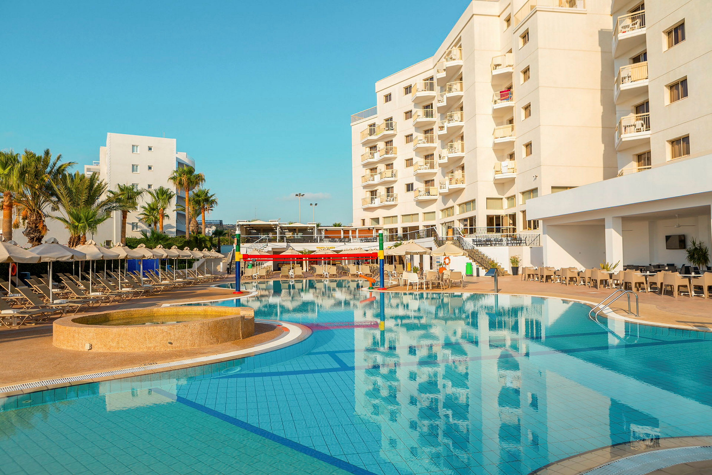 Hotellbyggnad vid en pool med solstolar och parasoller. (AI-genererad text)