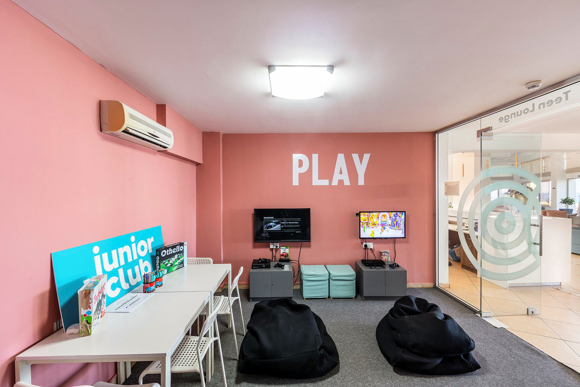Ett lekrum med rosa väggar, bord, stolar och spel samt sittsäckar, och texten 'PLAY' på väggen. (AI-genererad text)