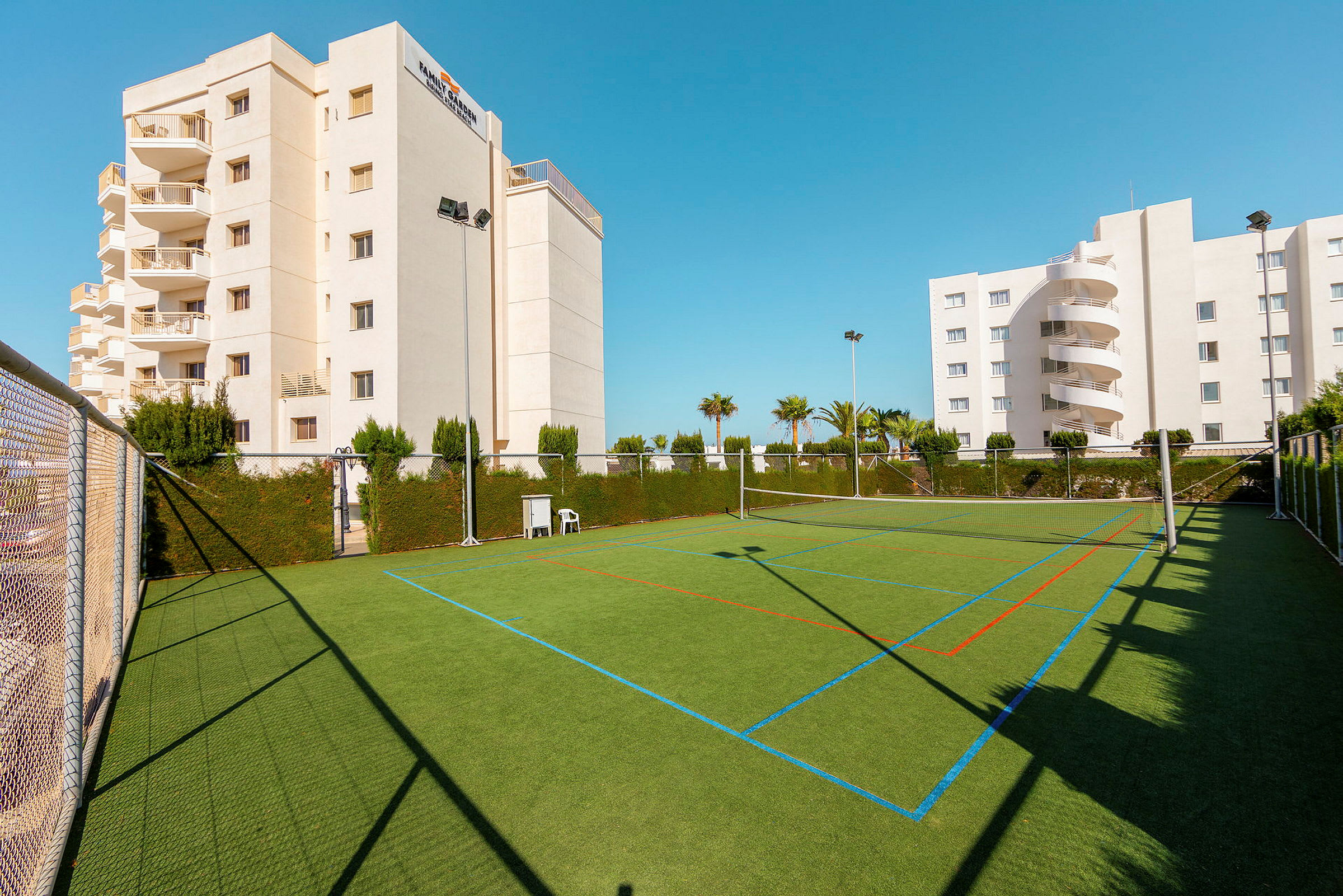 Fotbollsplan med grönt konstgräs, omgiven av staket och vegetation, i anslutning till hotellbyggnader. (AI-genererad text)