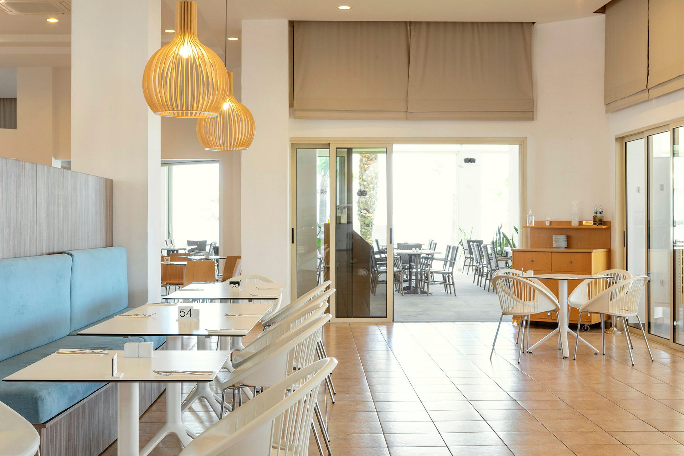 Interiör av en ljus restaurang med bord och stolar, samt taklampor. (AI-genererad text)