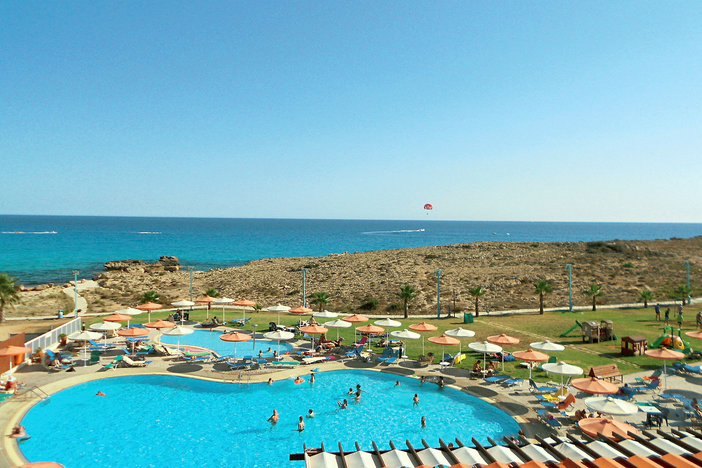 En pool med solstolar under parasoller vid havet. (AI-genererad text)
