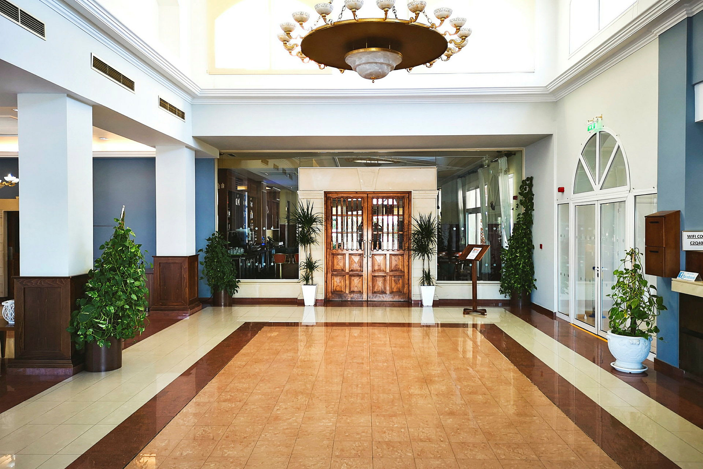 En hotellobby med trädetaljer, stora glasdörrar och gröna växter. (AI-genererad text)