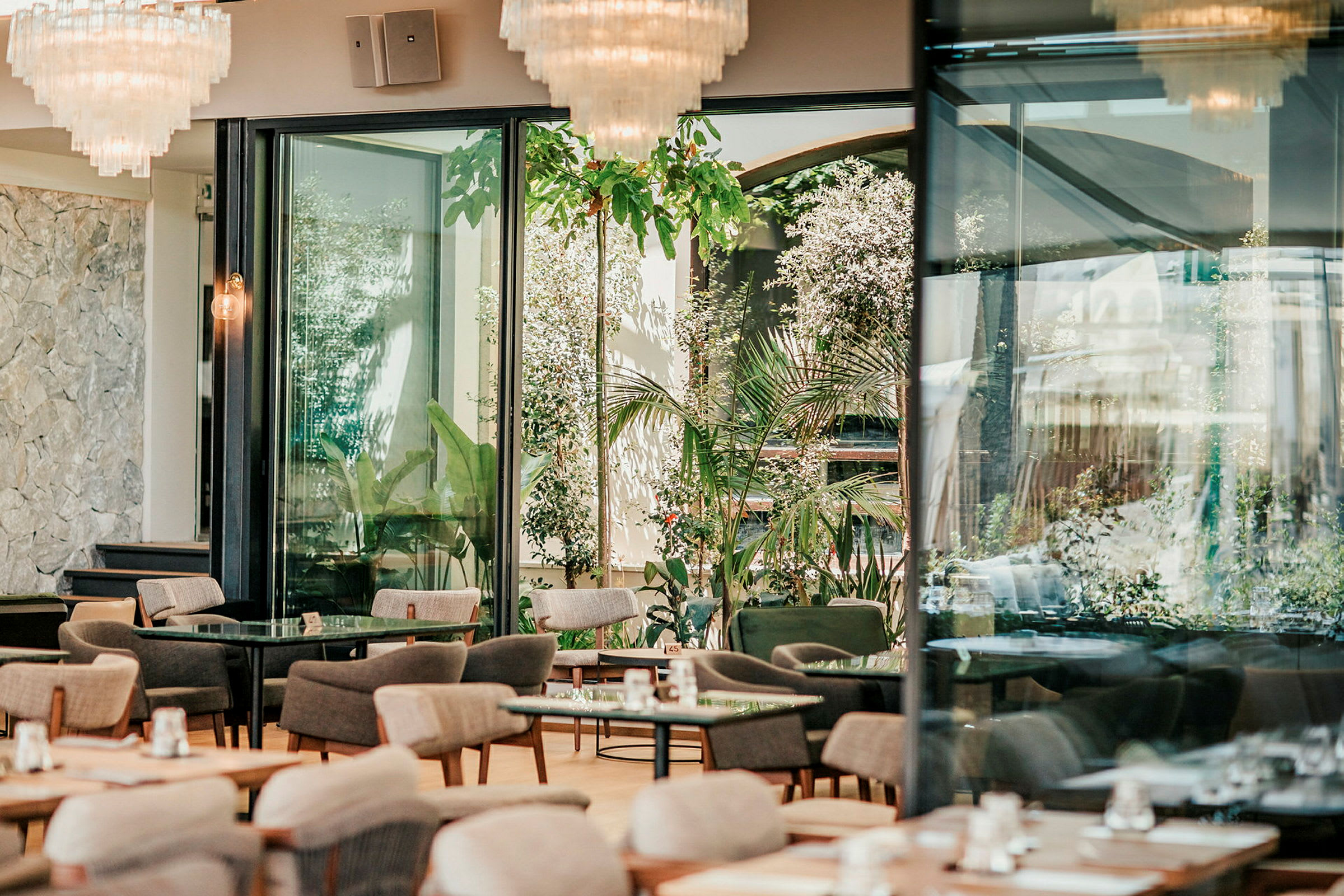 En modern, välbelyst restaurang med stora fönster och grönska utanför. (AI-genererad text)