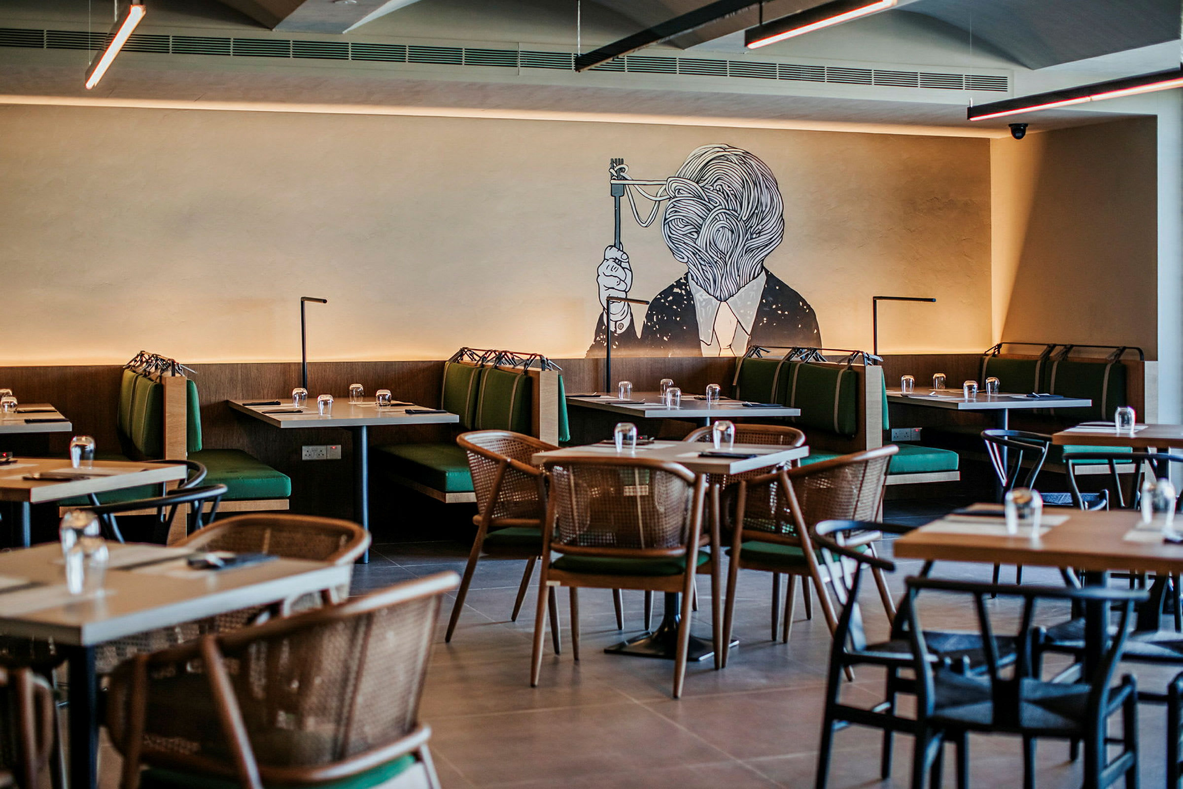En restaurang med bord och gröna soffor samt en väggmålning av ett konstverk. (AI-genererad text)