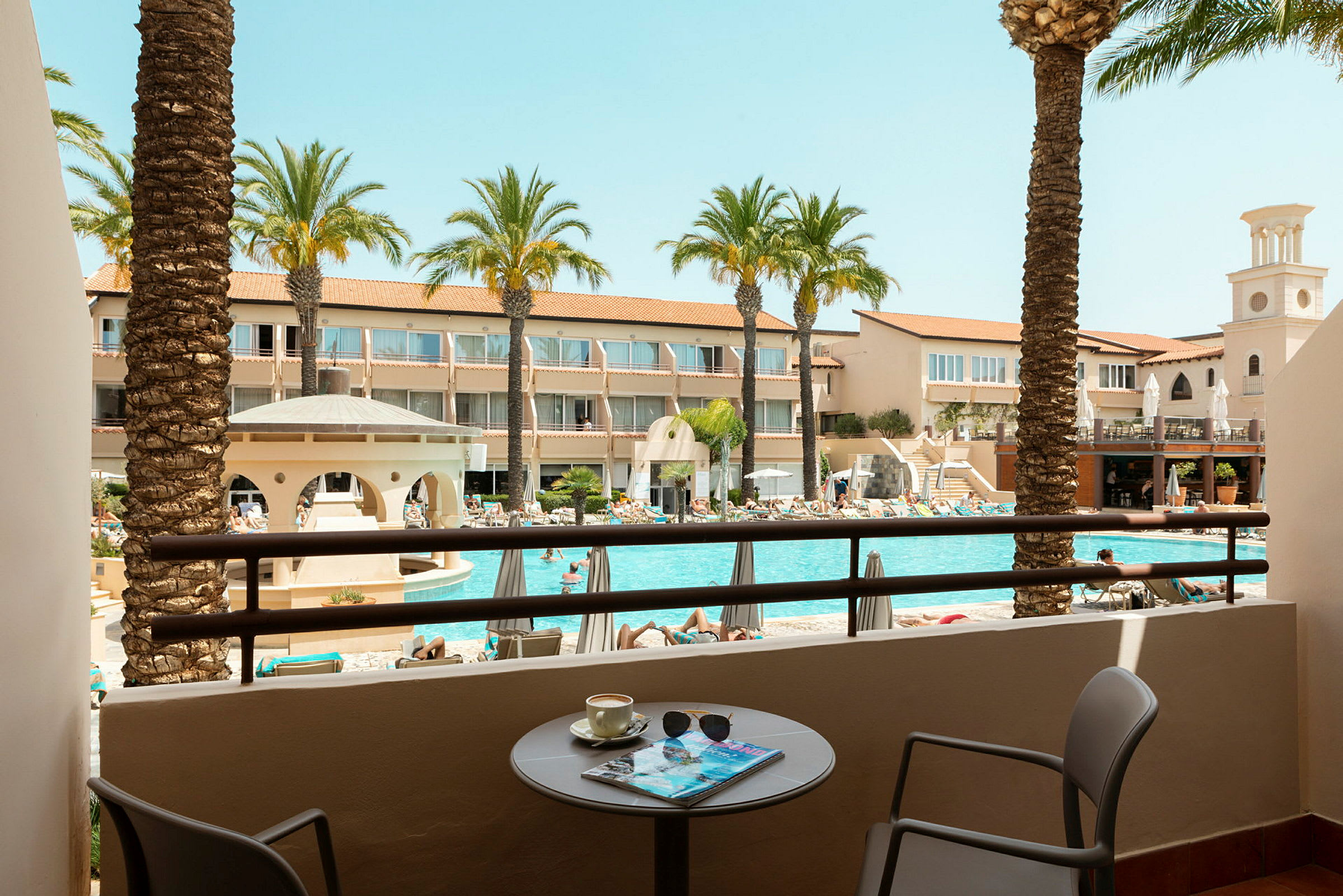Vy från en balkong över en pool och omgivande hotellbyggnader. (AI-genererad text)
