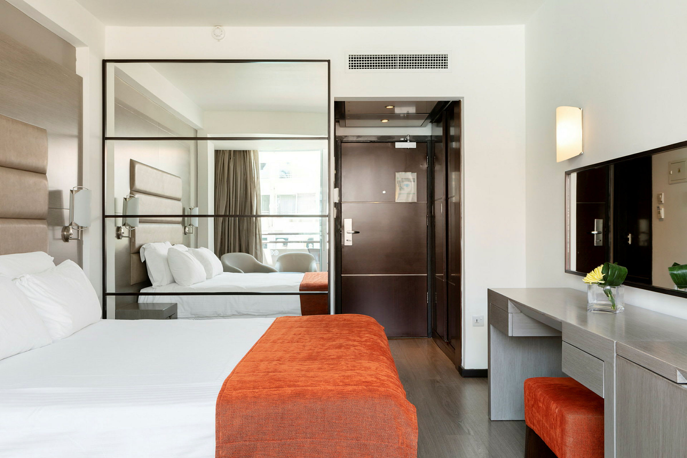 Hotellrum med en säng, en spegel, en skrivbord och dörr. (AI-genererad text)