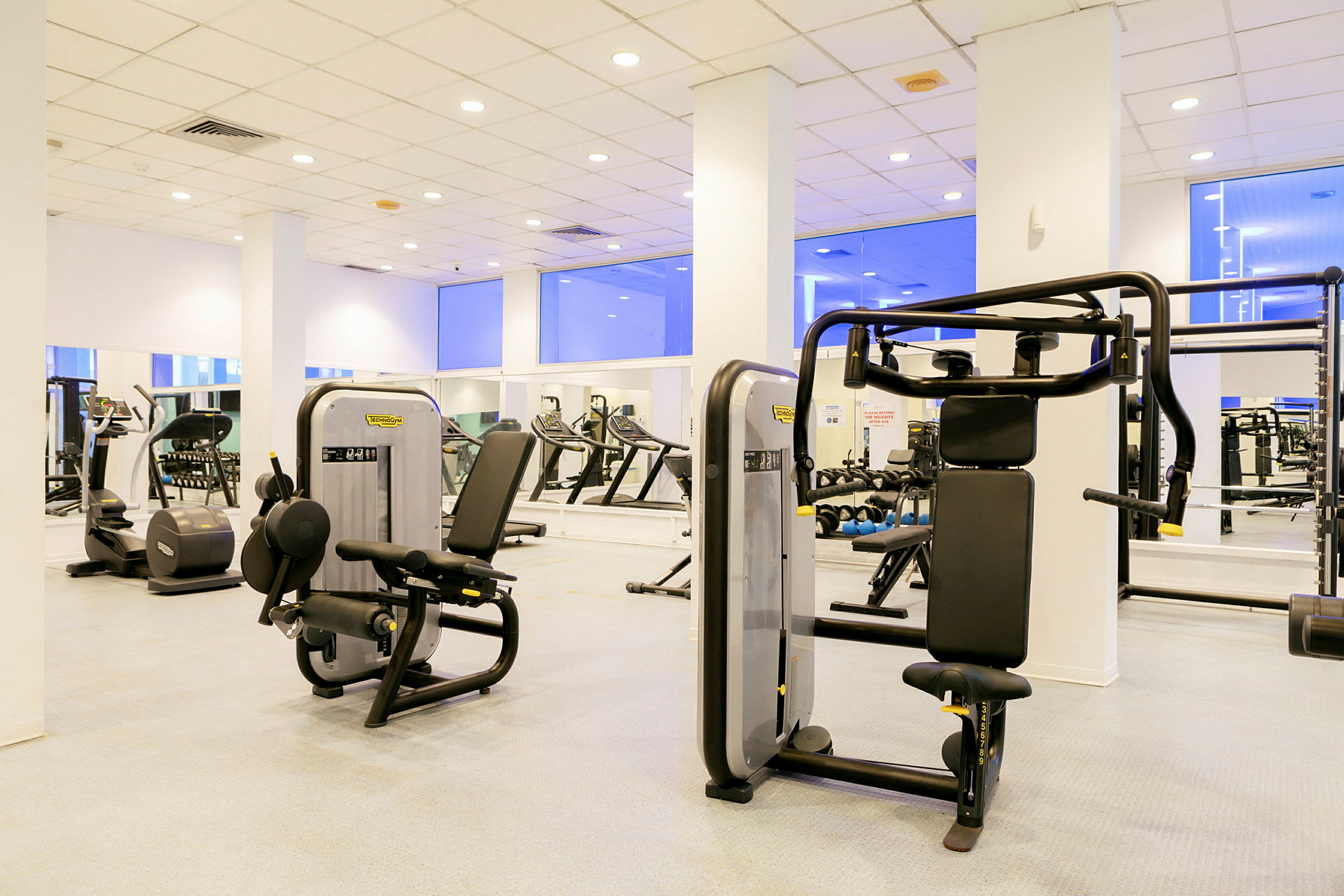 Ett gym med träningsmaskiner och speglar längs väggarna. (AI-genererad text)