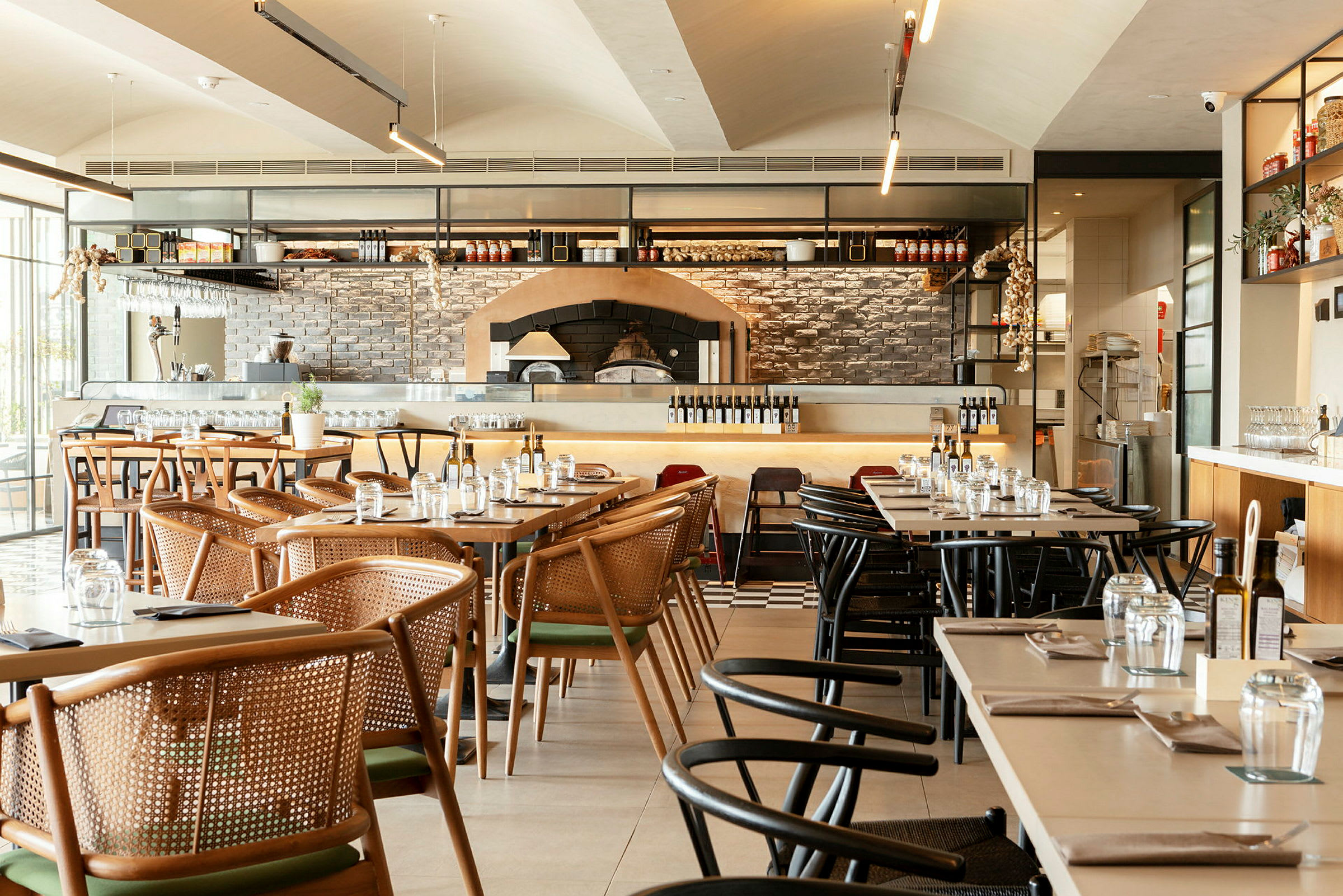 En restaurang med dukade bord och stolar samt synlig pizzaugn. (AI-genererad text)