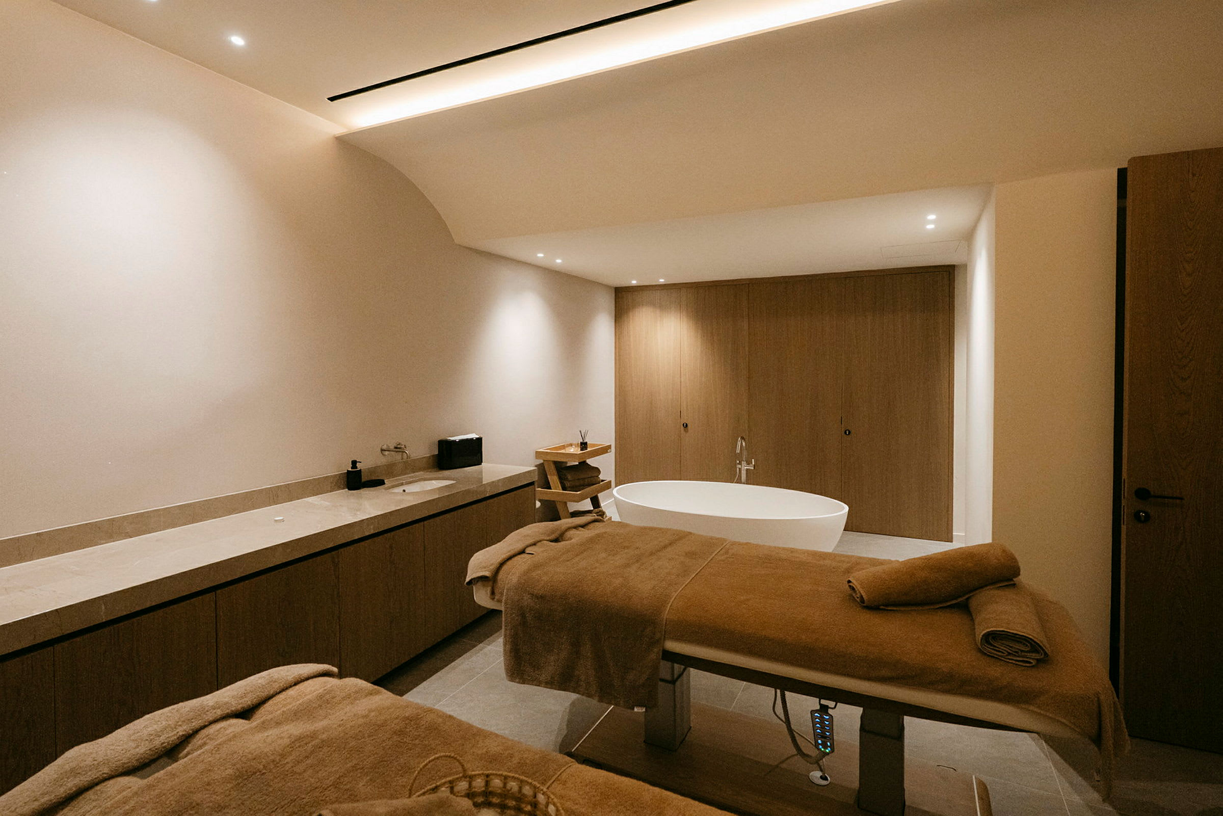 Ett modernt spa-rum med två massagebänkar, en fristående badkar och träinredning. (AI-genererad text)