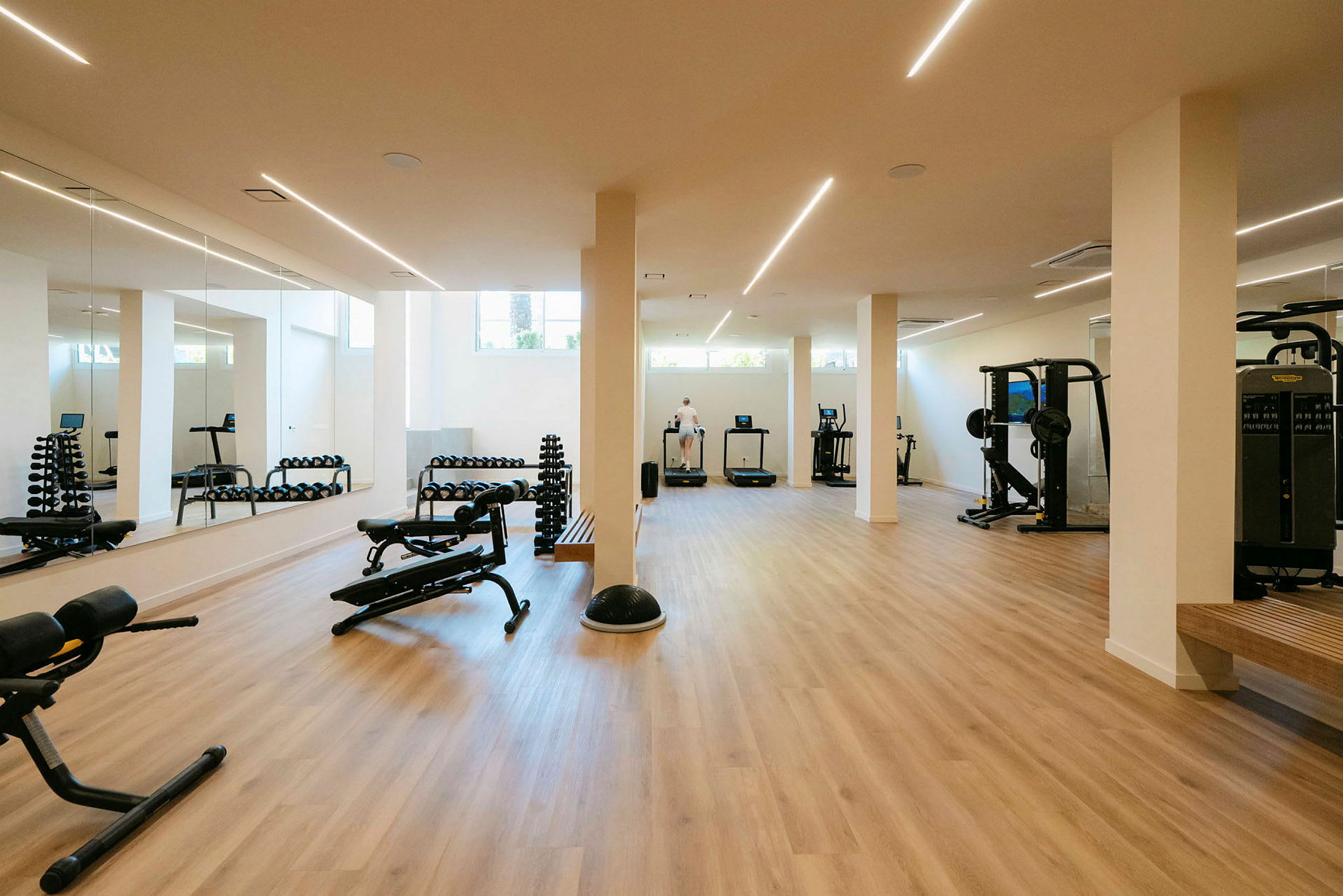 Ett gym med träningsmaskiner och hantlar, spegelbeklädda väggar och ljust trägolv. (AI-genererad text)