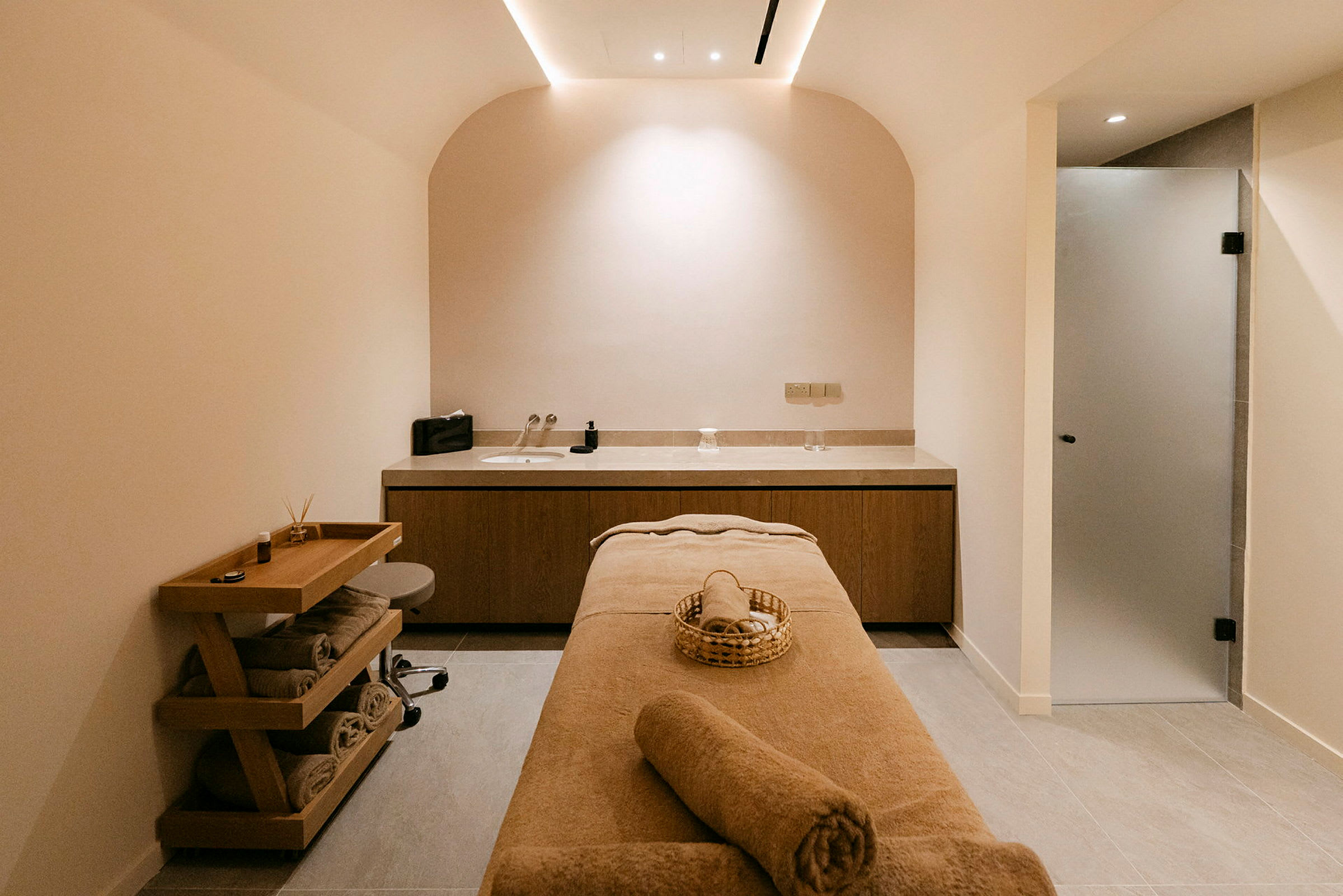 Ett spa-rum med en massagebänk, träbänk för förvaring, och en handfatssektion med ljusa nyanser. (AI-genererad text)