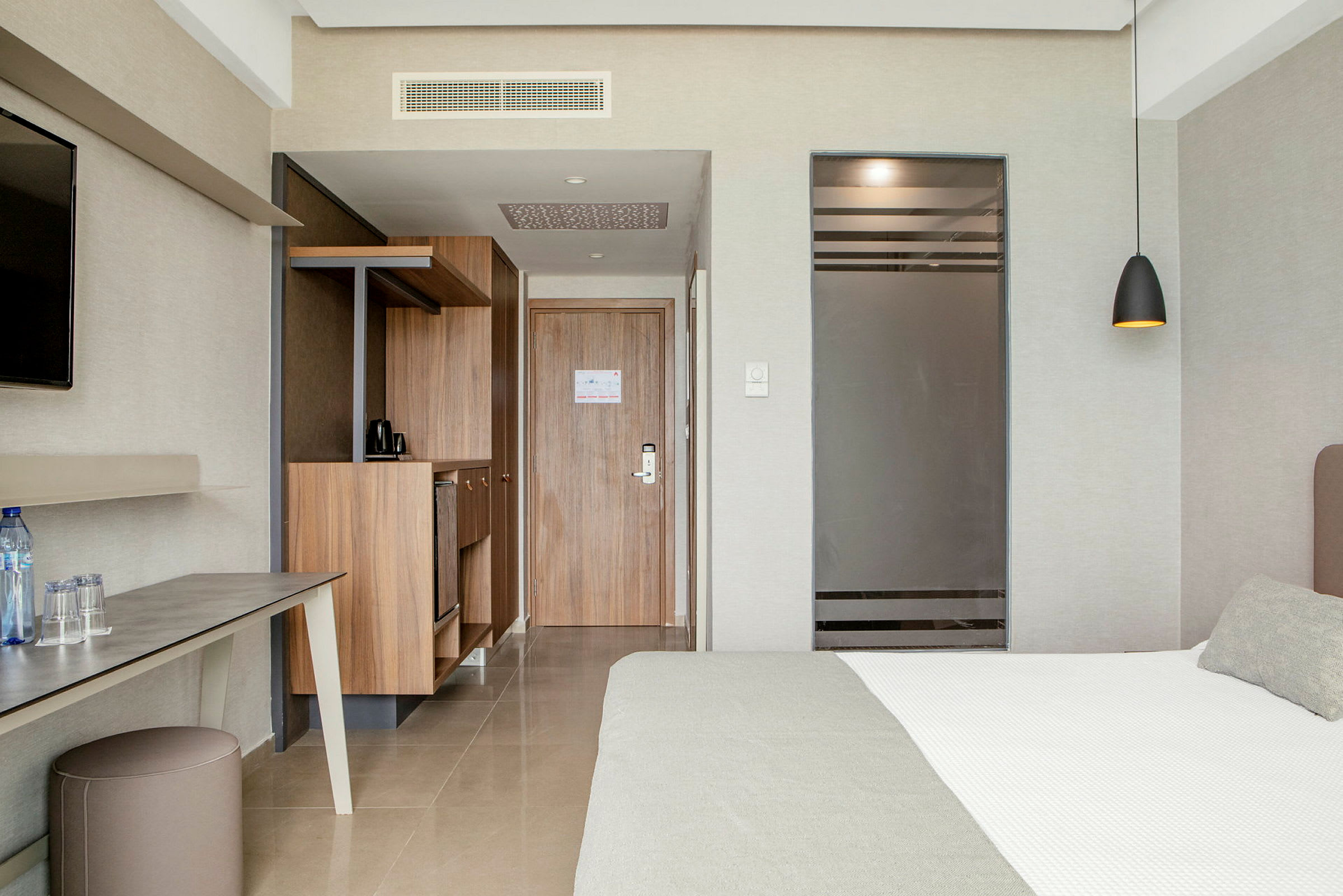 Hotellrum med synlig säng, skrivbord, förvaringsutrymme och en dörr. (AI-genererad text)