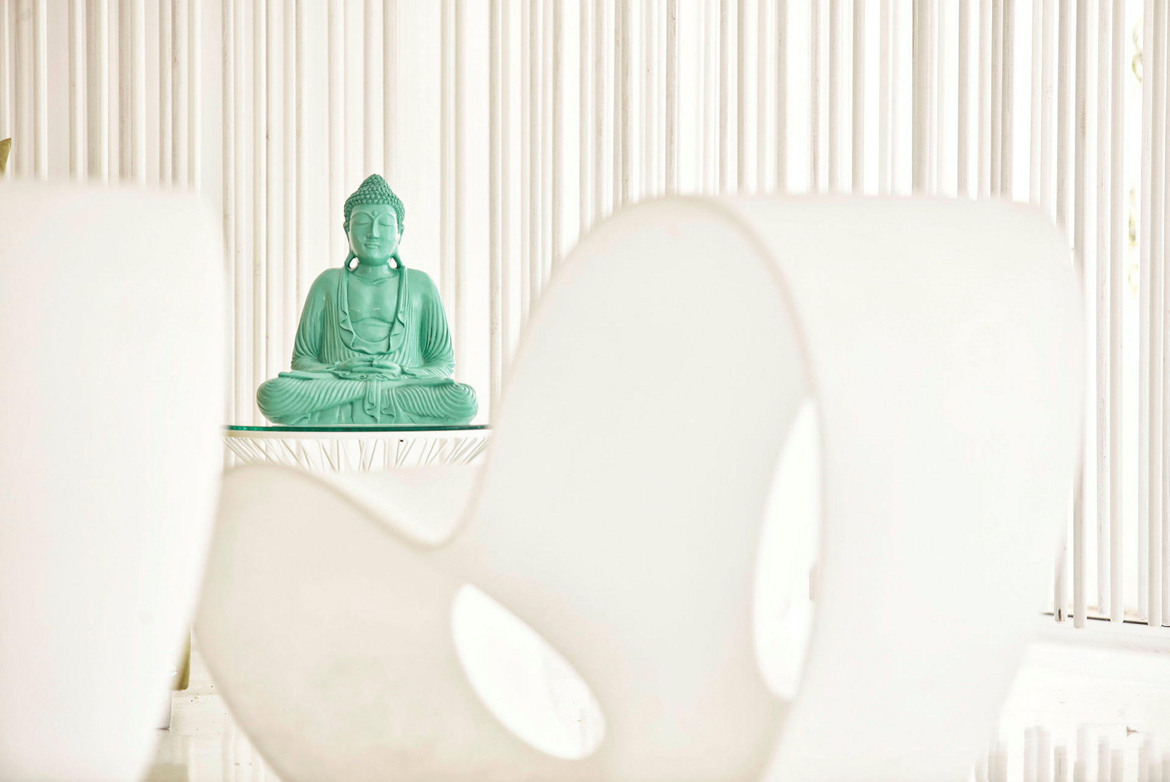 En grön Buddha-staty placerad på ett bord mot en minimalistisk bakgrund. (AI-genererad text)