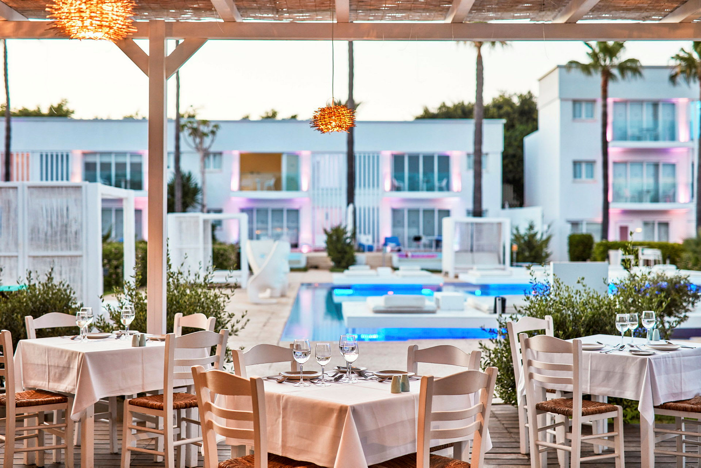 Restaurang med dukade bord vid pool med moderna byggnader i bakgrunden. (AI-genererad text)