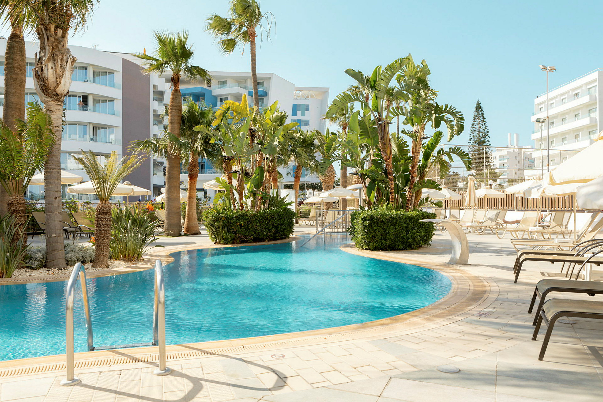 En pool omgiven av solstolar och palmer vid ett hotell. (AI-genererad text)