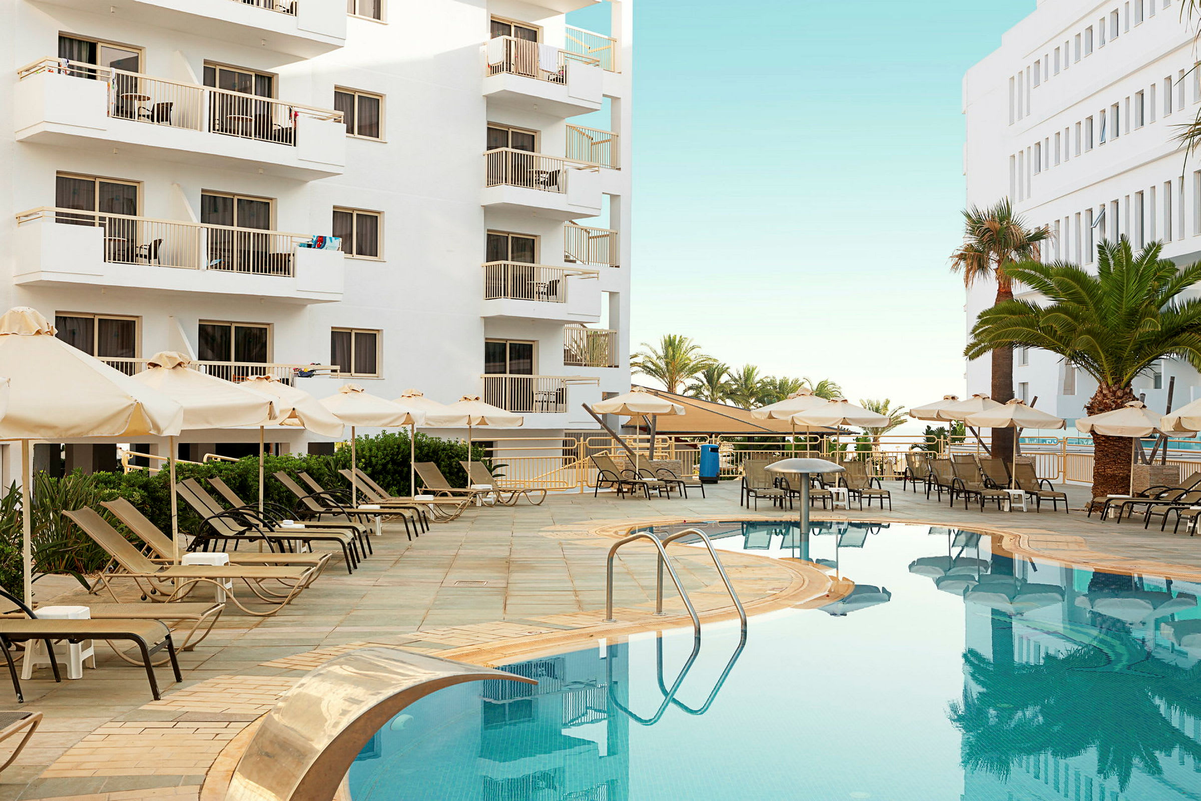 Bild av ett hotellpoolområde med solstolar, parasoll och vita byggnader i bakgrunden. (AI-genererad text)