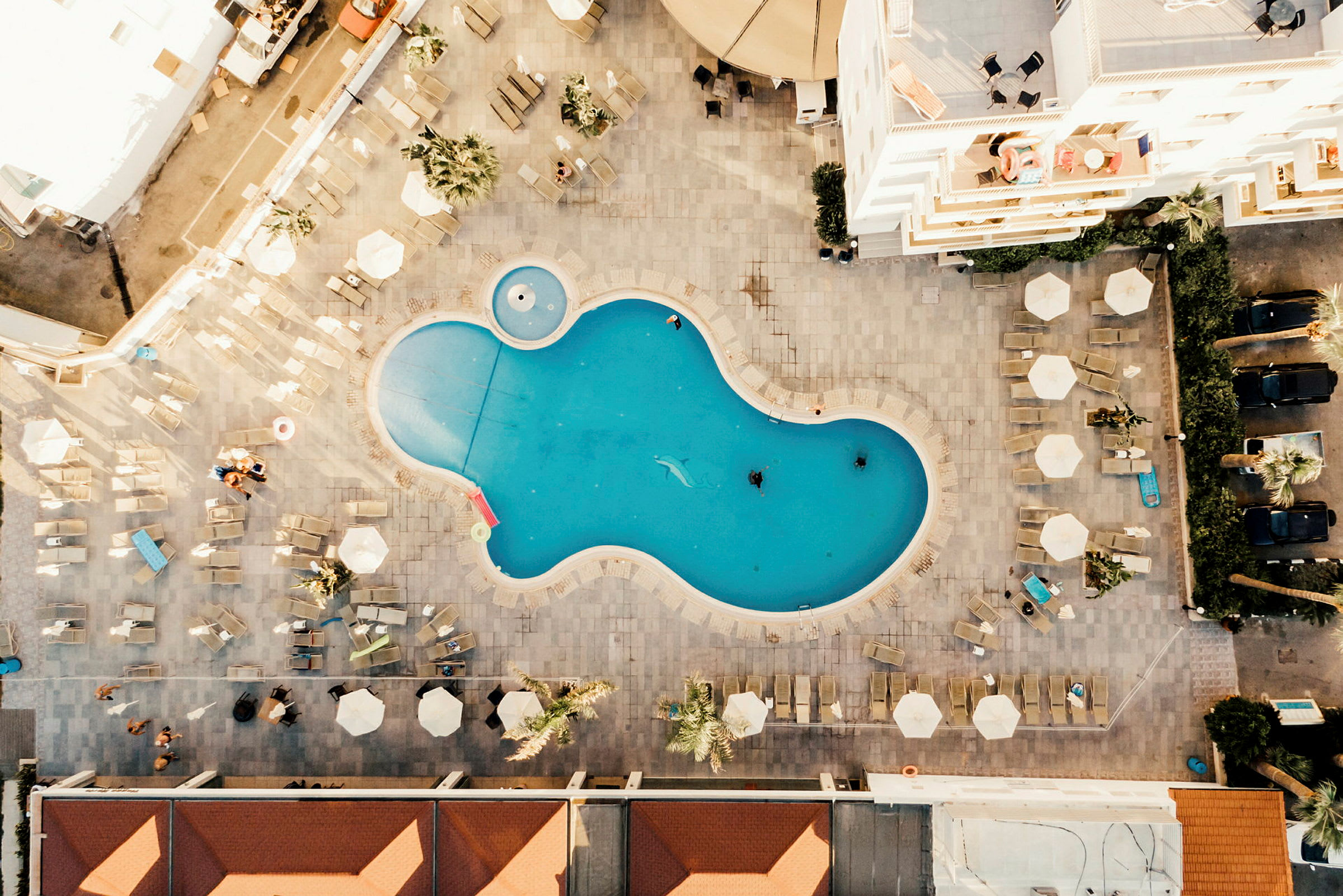 Flygfoto av en friformad swimmingpool omgiven av solstolar och parasoller. (AI-genererad text)