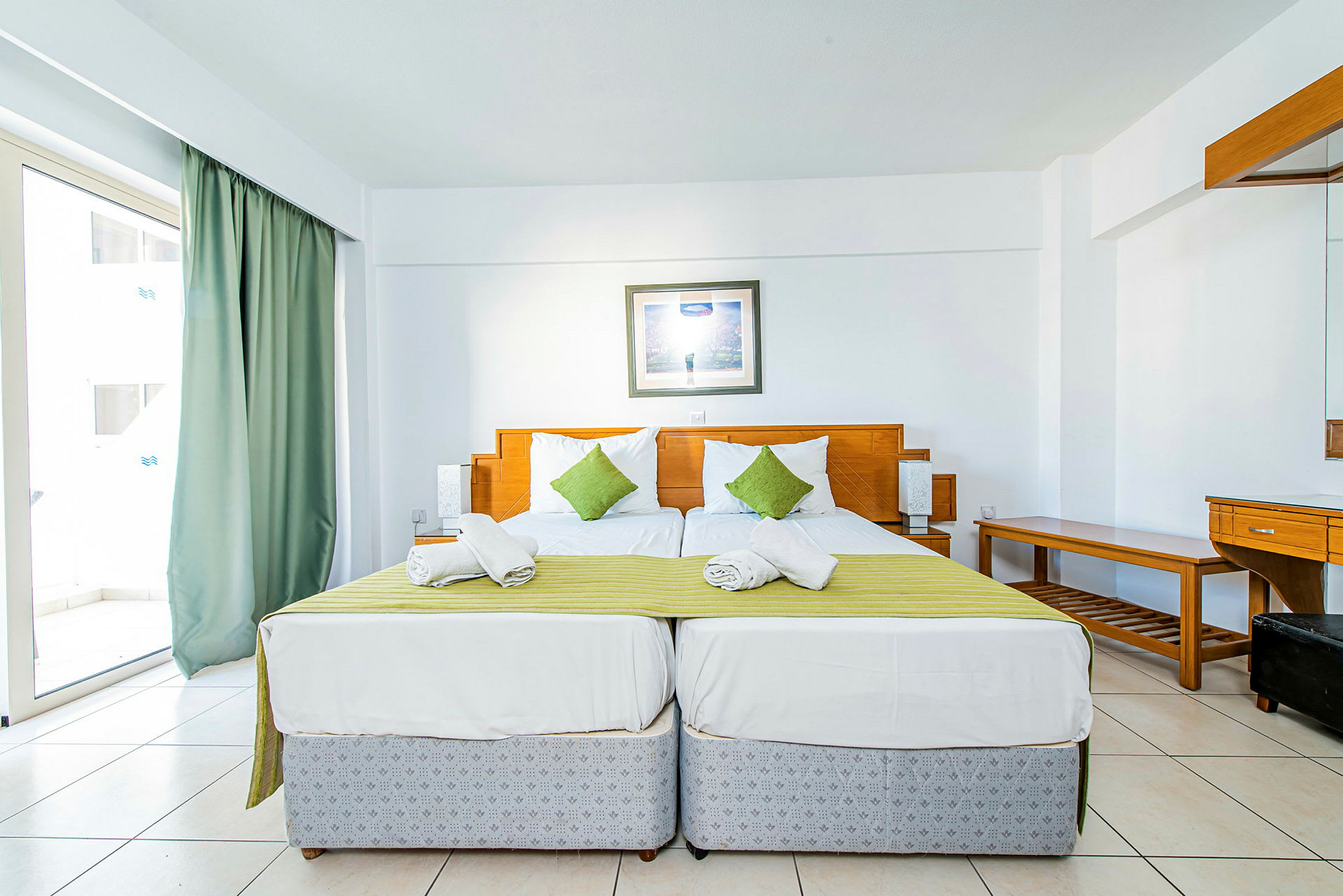 Två enkelsängar med grön överkast och vita kuddar i ett hotellrum med ljus inredning. (AI-genererad text)