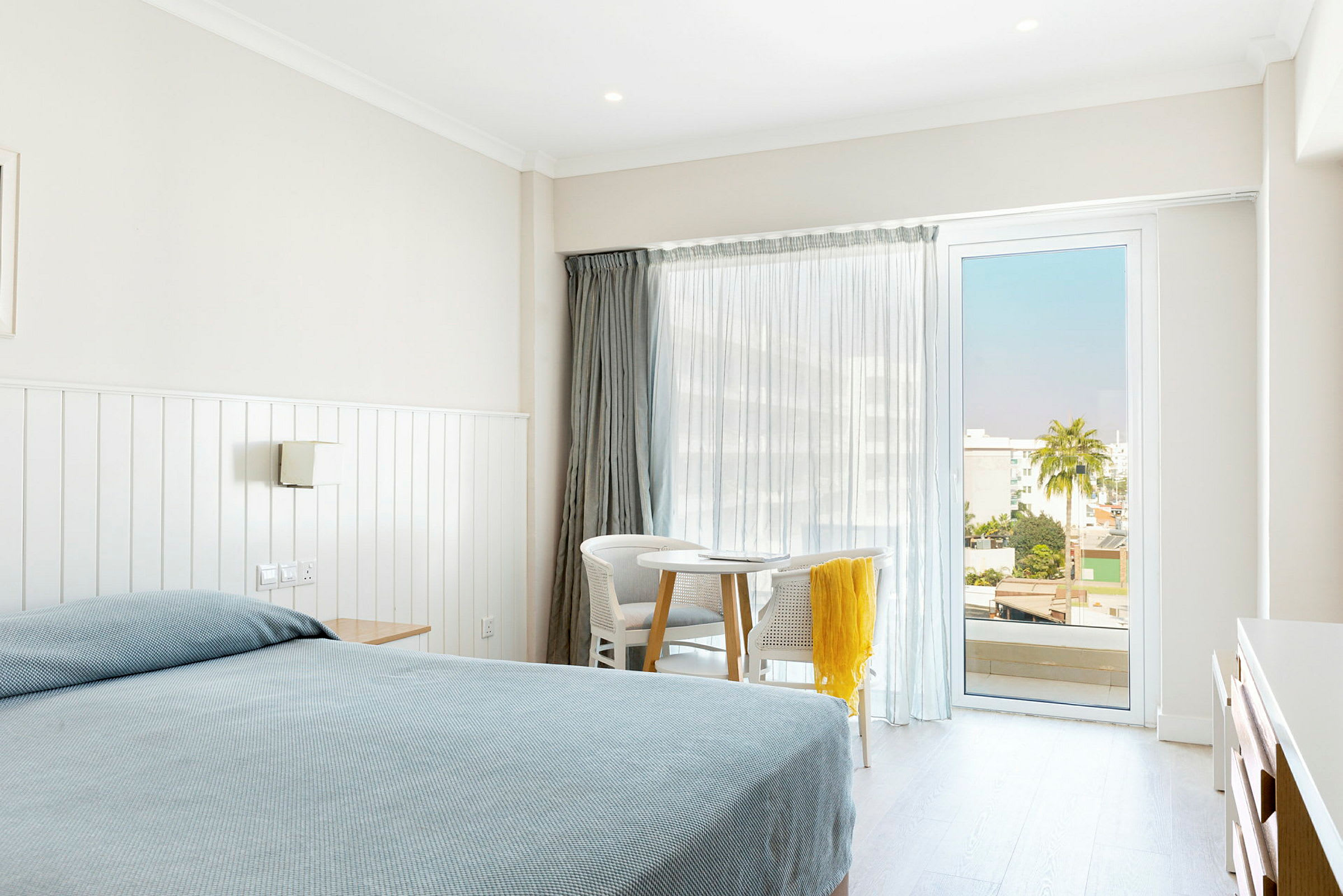 Ett hotellrum med en säng, ett bord och två stolar framför ett glasfönster. (AI-genererad text)