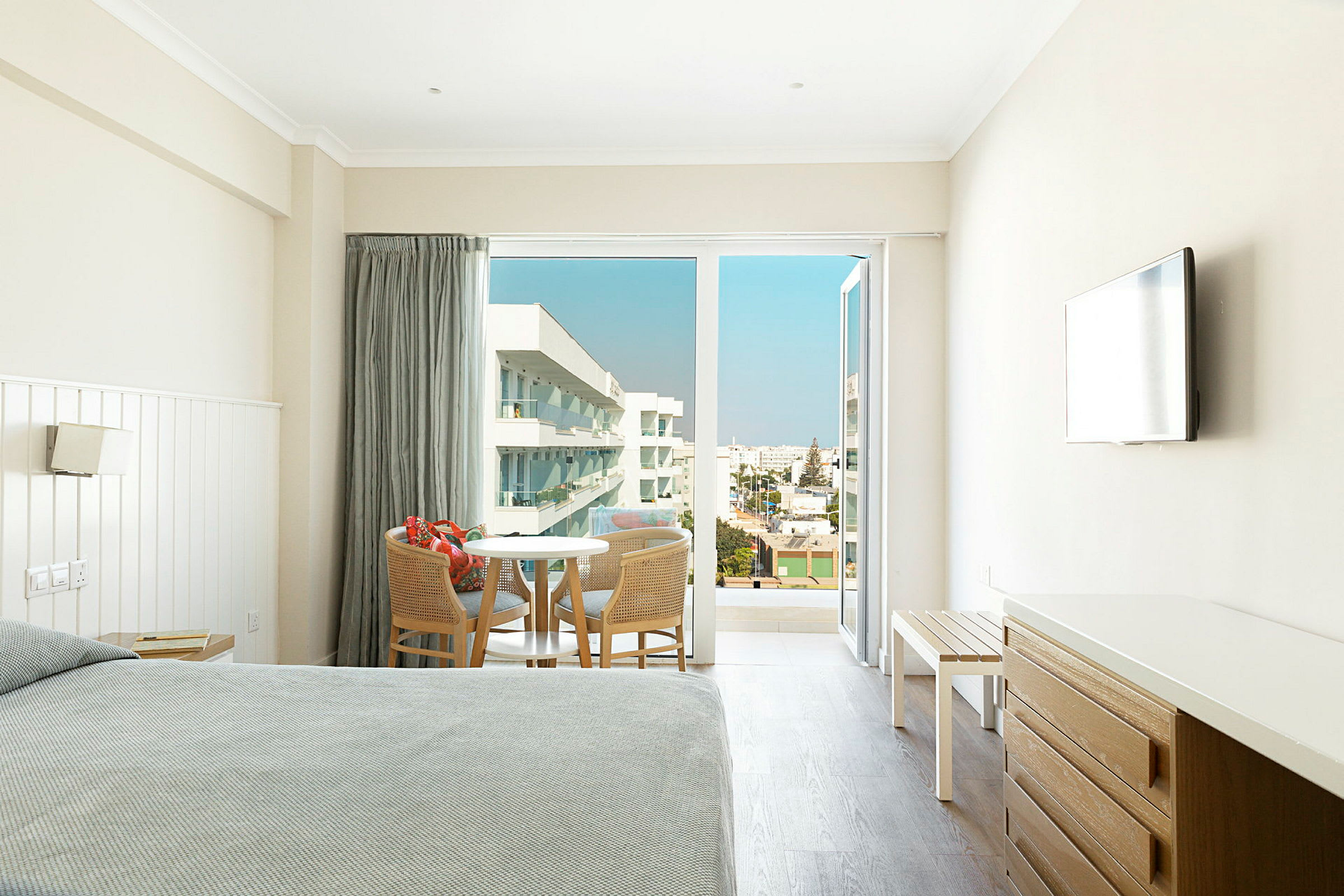Hotellrum med sittgrupp och öppna balkongdörrar med utsikt över omgivningen. (AI-genererad text)