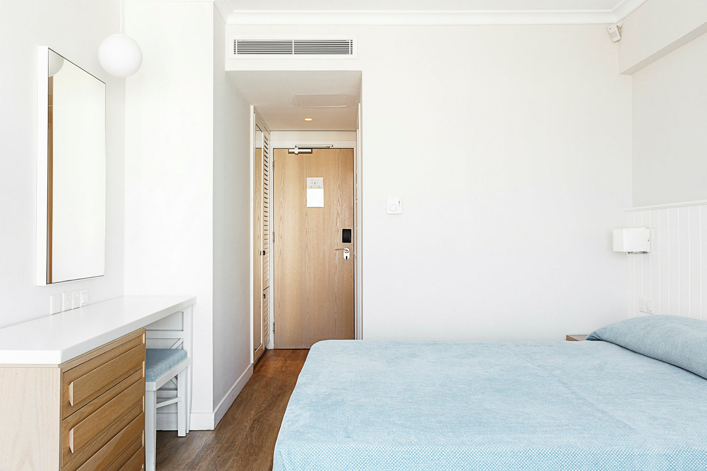 Ett hotellrum med en säng, en spegel på en byrå och en dörr. (AI-genererad text)