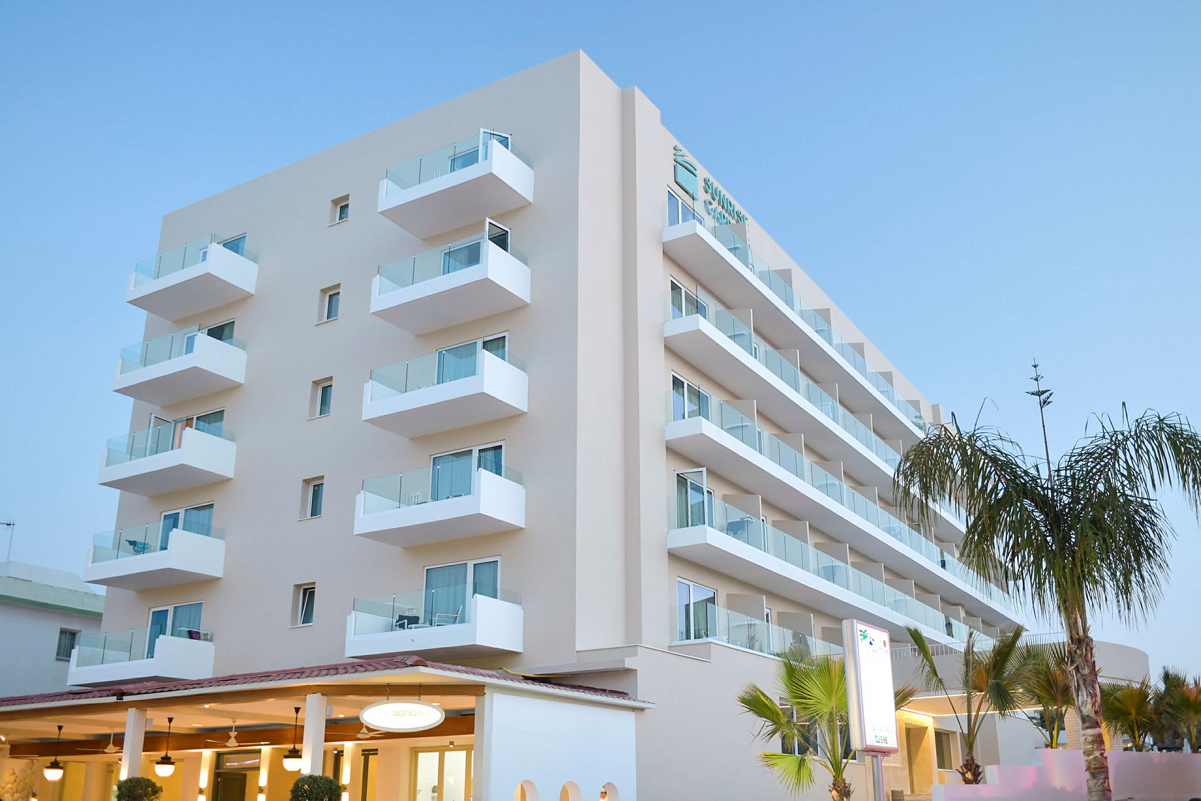 Ett modernt hotell med flera våningar och balkonger, omgivet av palmträd. (AI-genererad text)