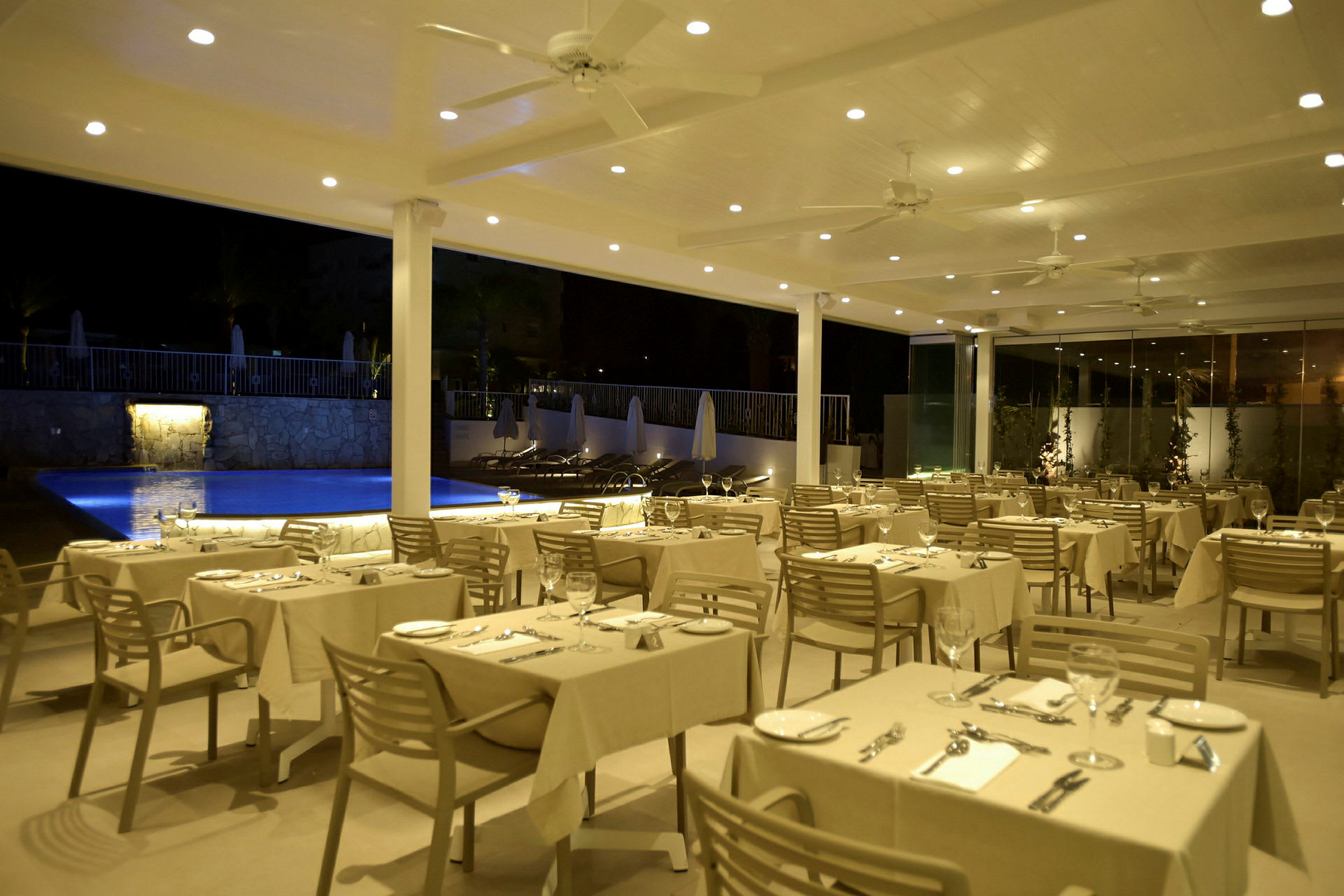 Restaurang med uppdukade bord nära en pool på kvällstid. (AI-genererad text)