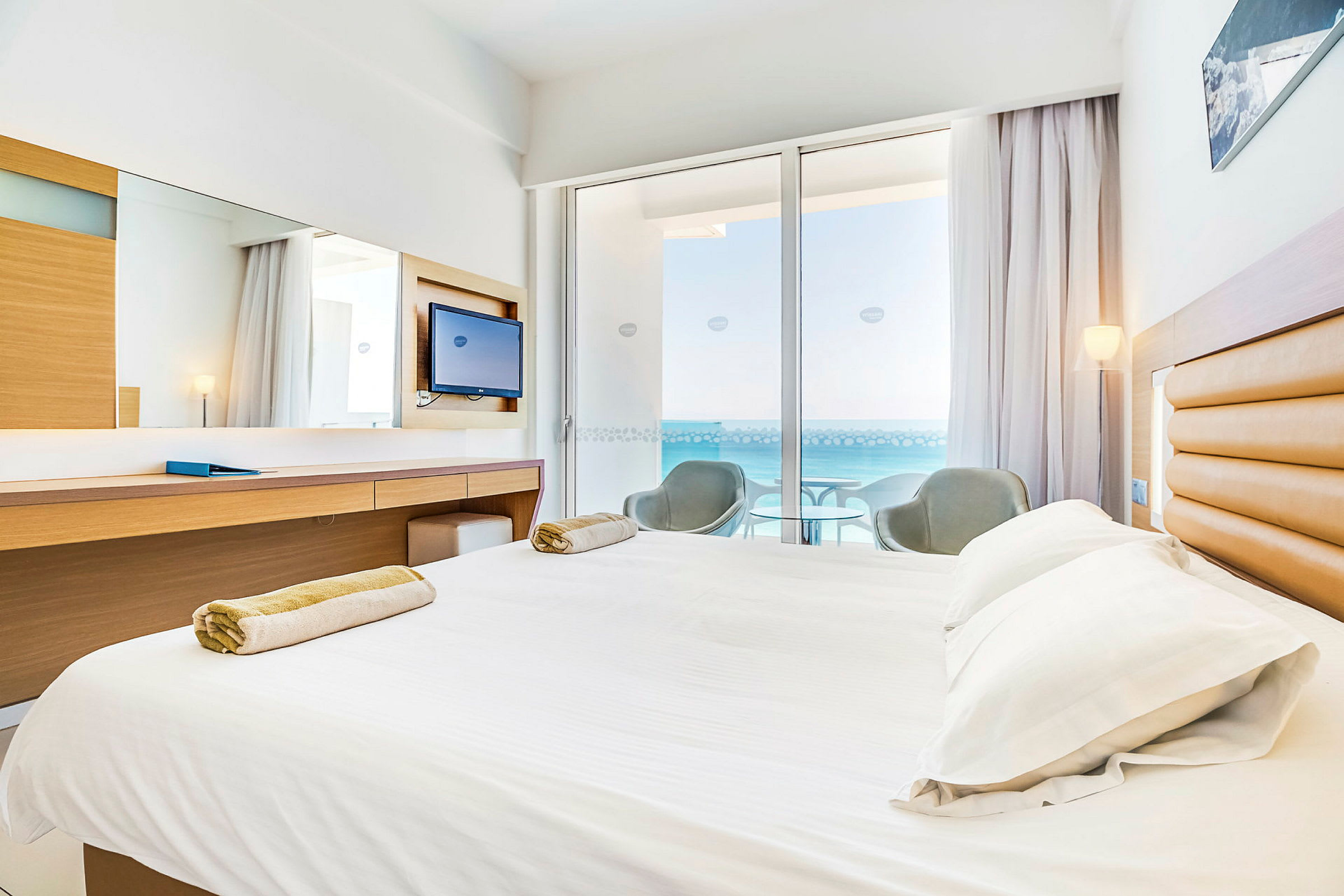 Hotellrum med säng, skrivbord och balkong med utsikt över havet. (AI-genererad text)
