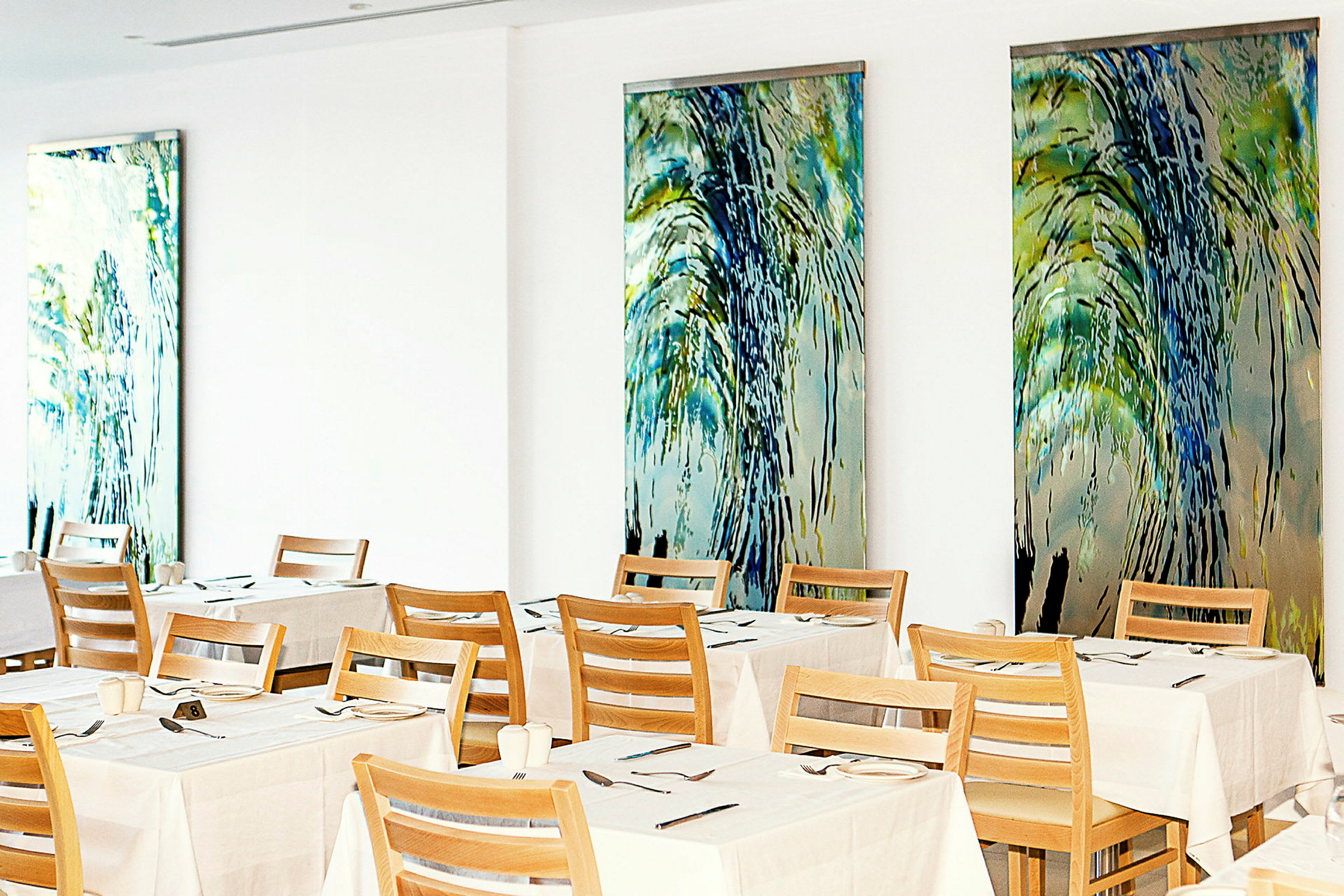En restaurang med uppdukade bord och trästolar mot väggar dekorerade med färgglada konstverk. (AI-genererad text)