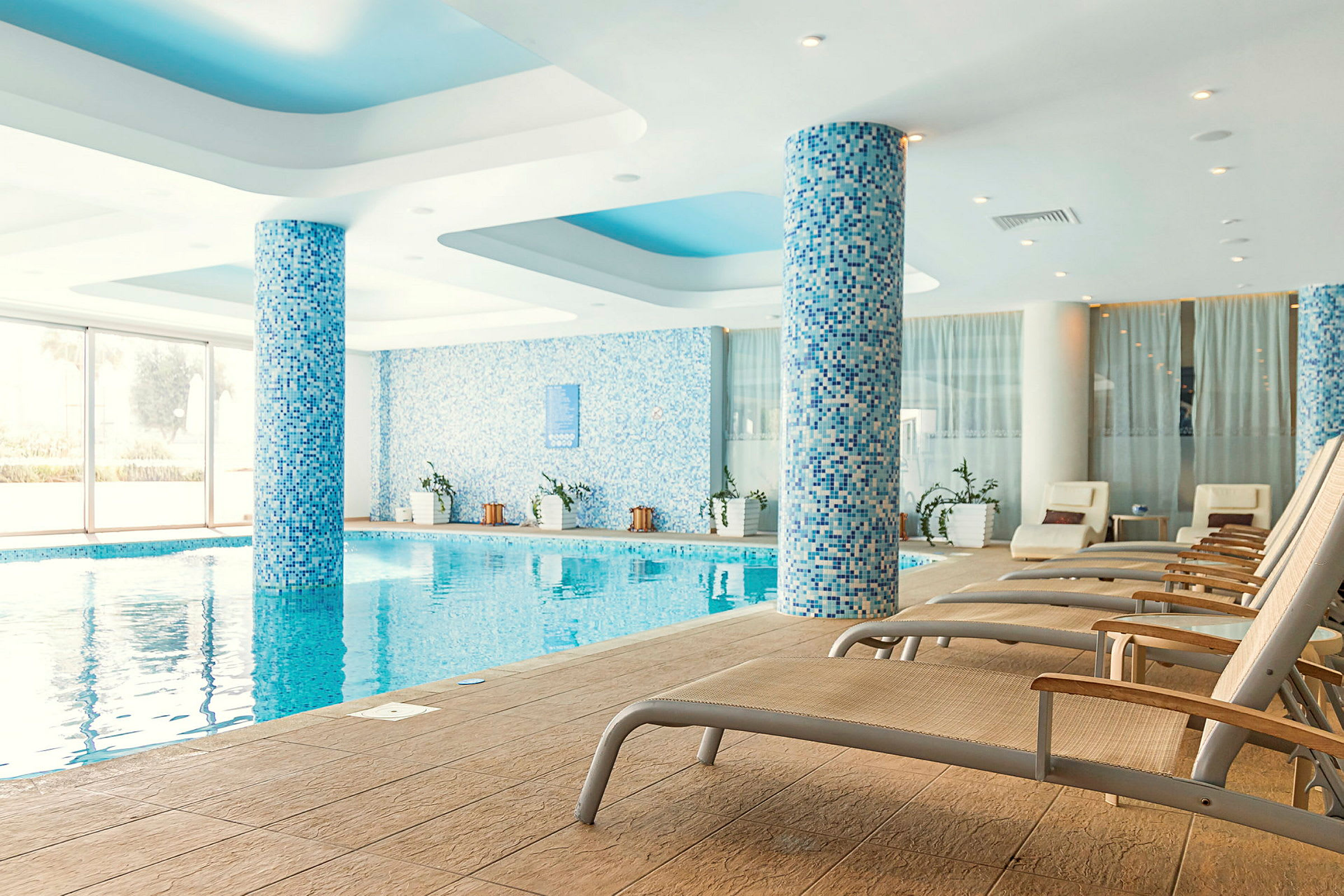 En inomhuspool med solsängar och pelare täckta av blå mosaik. (AI-genererad text)