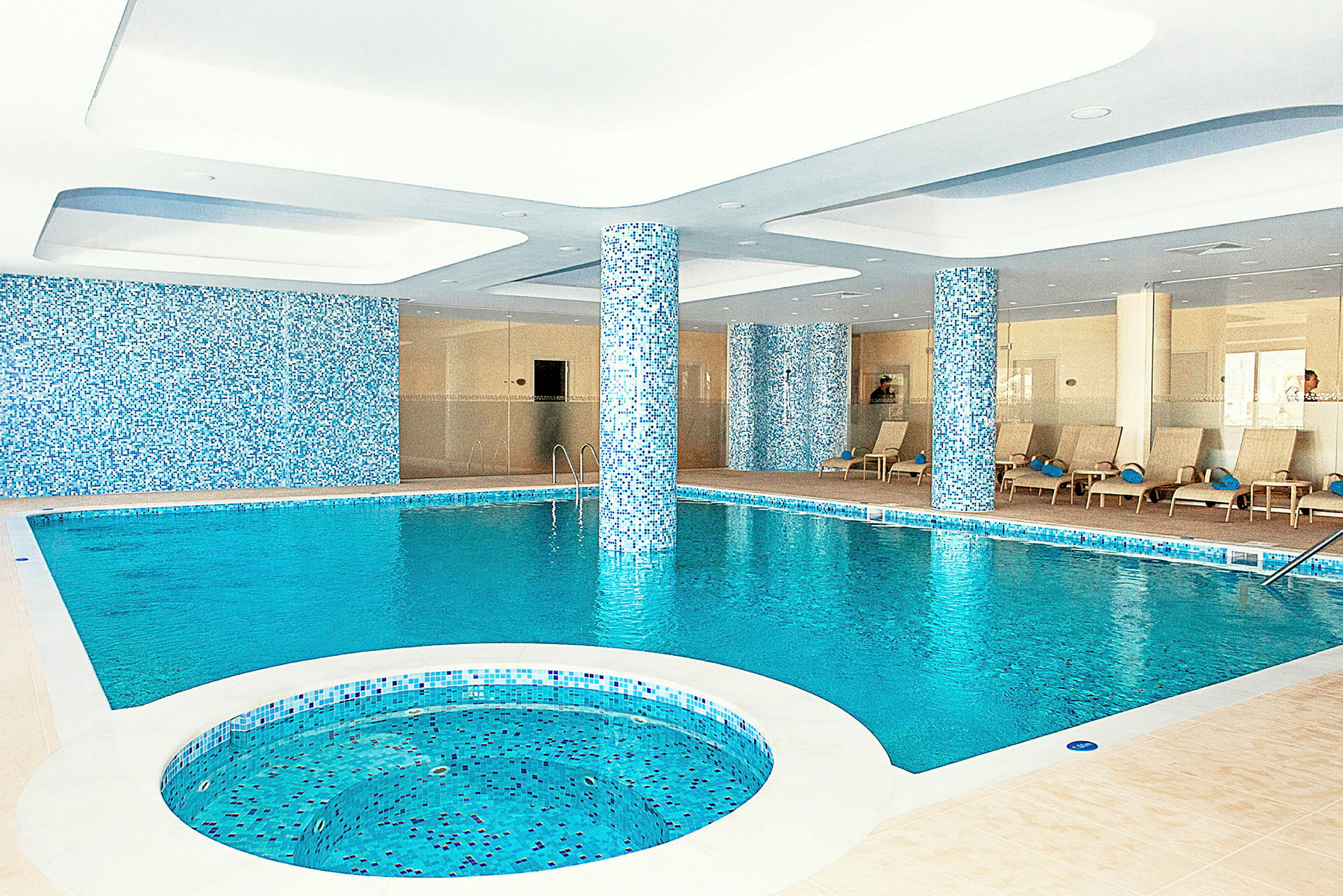 Inomhuspool med sittområde och pelare dekorerade med mosaik. (AI-genererad text)